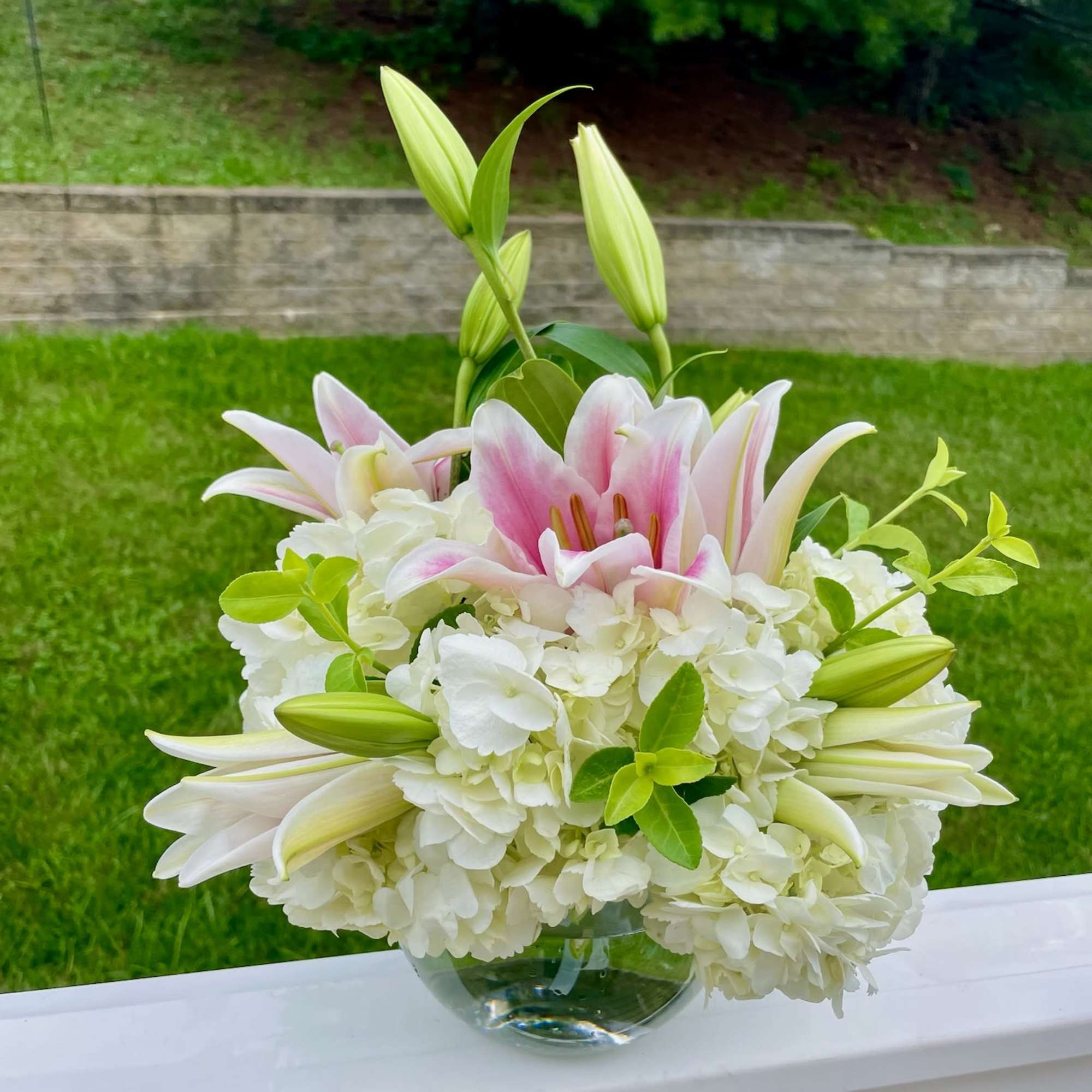White hydrangeas and pink lilies arranged in a glass vase