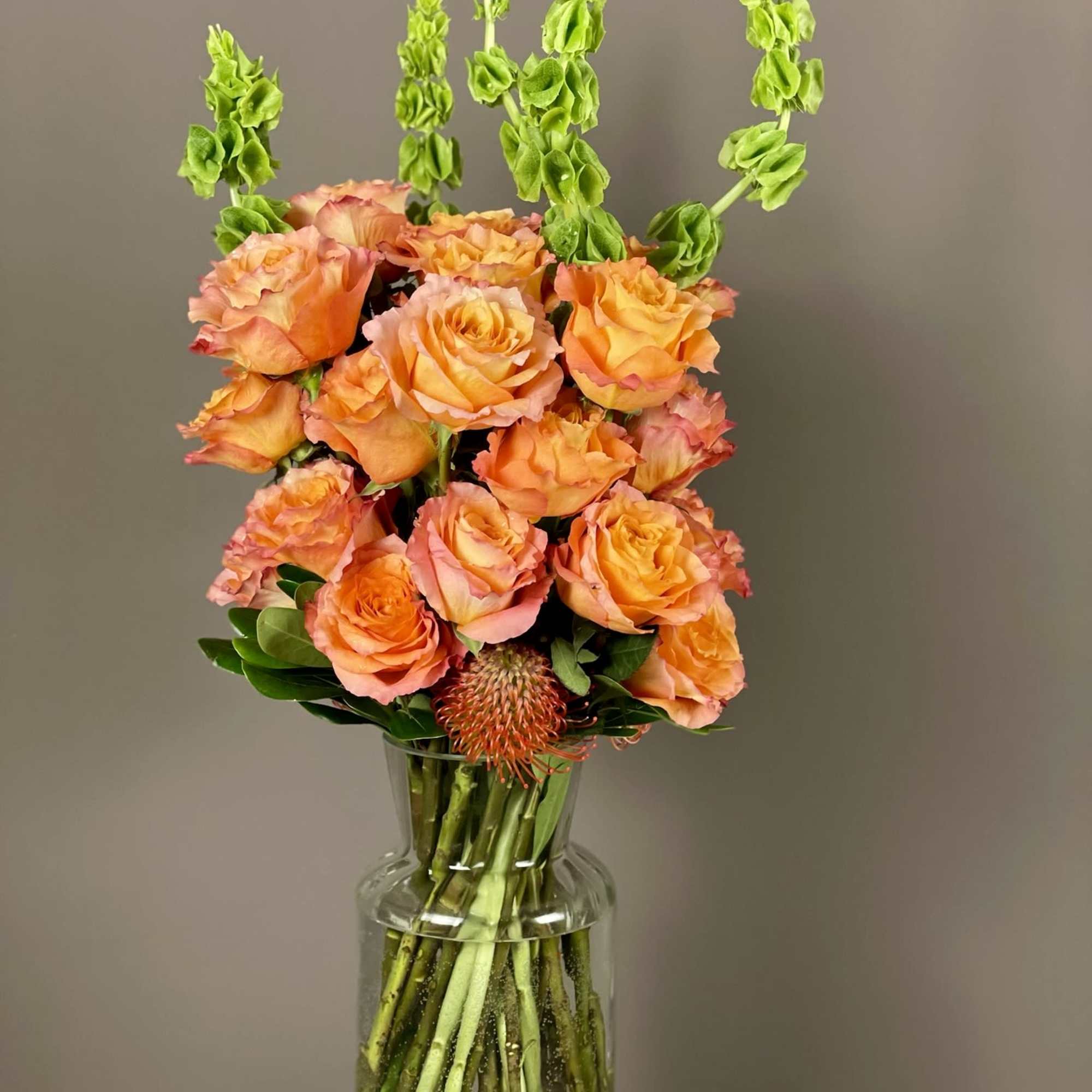 Orange roses in a clear glass vase with tall green spikes
