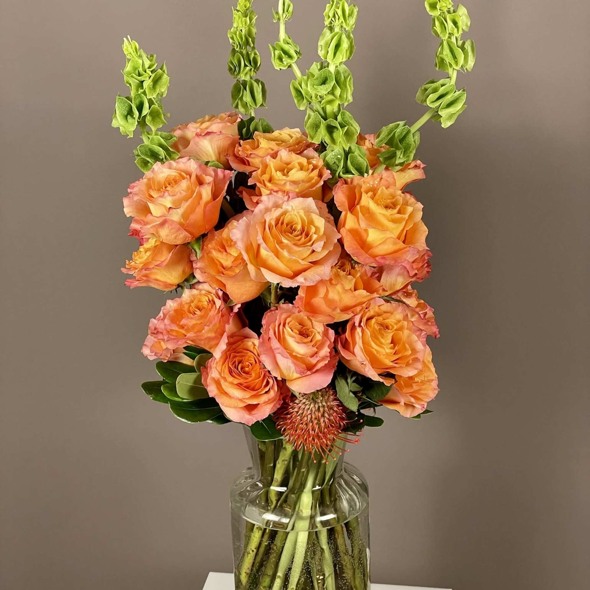 Orange roses in a clear glass vase with tall green spikes, photo 3 of 4