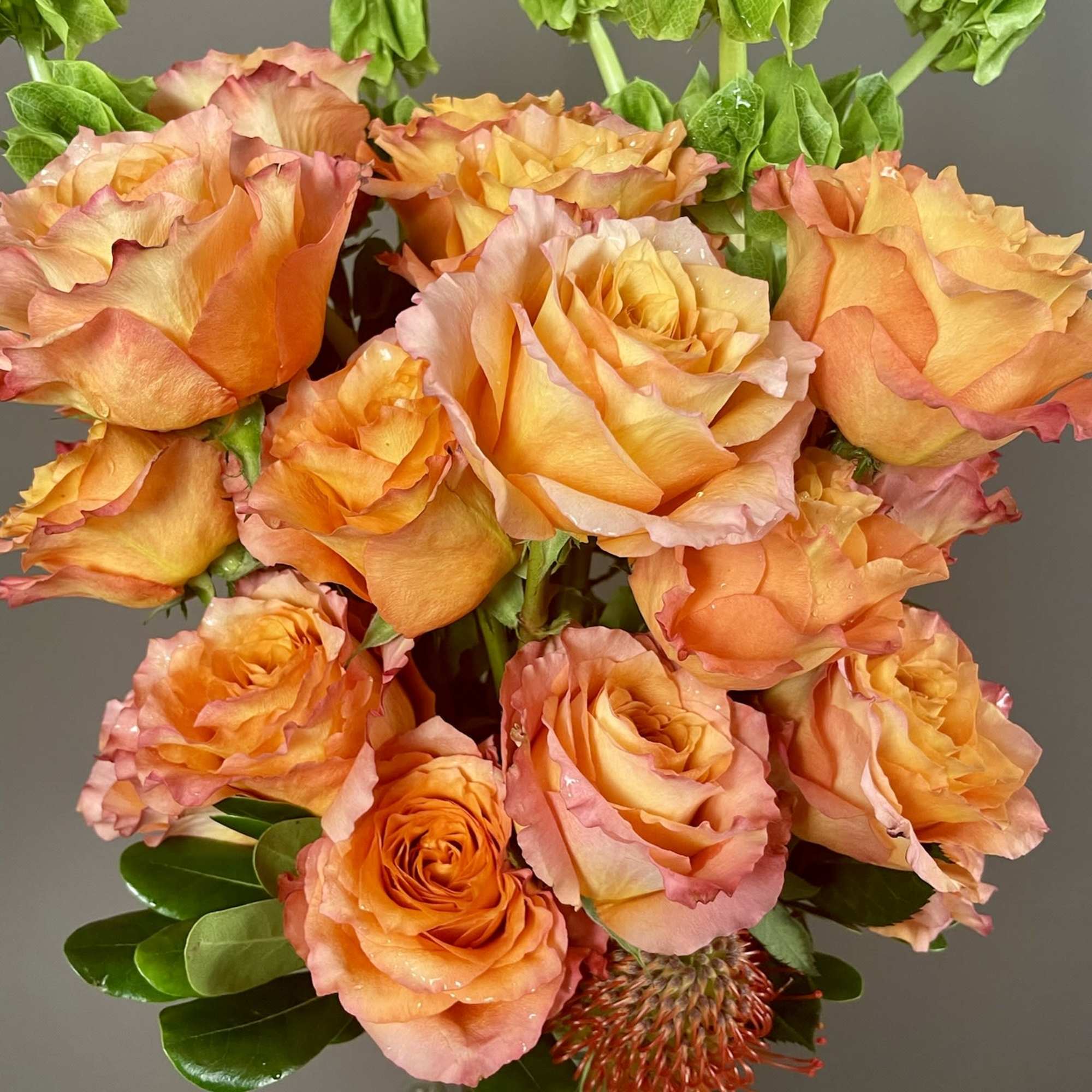 Orange roses in a glass vase with green foliage