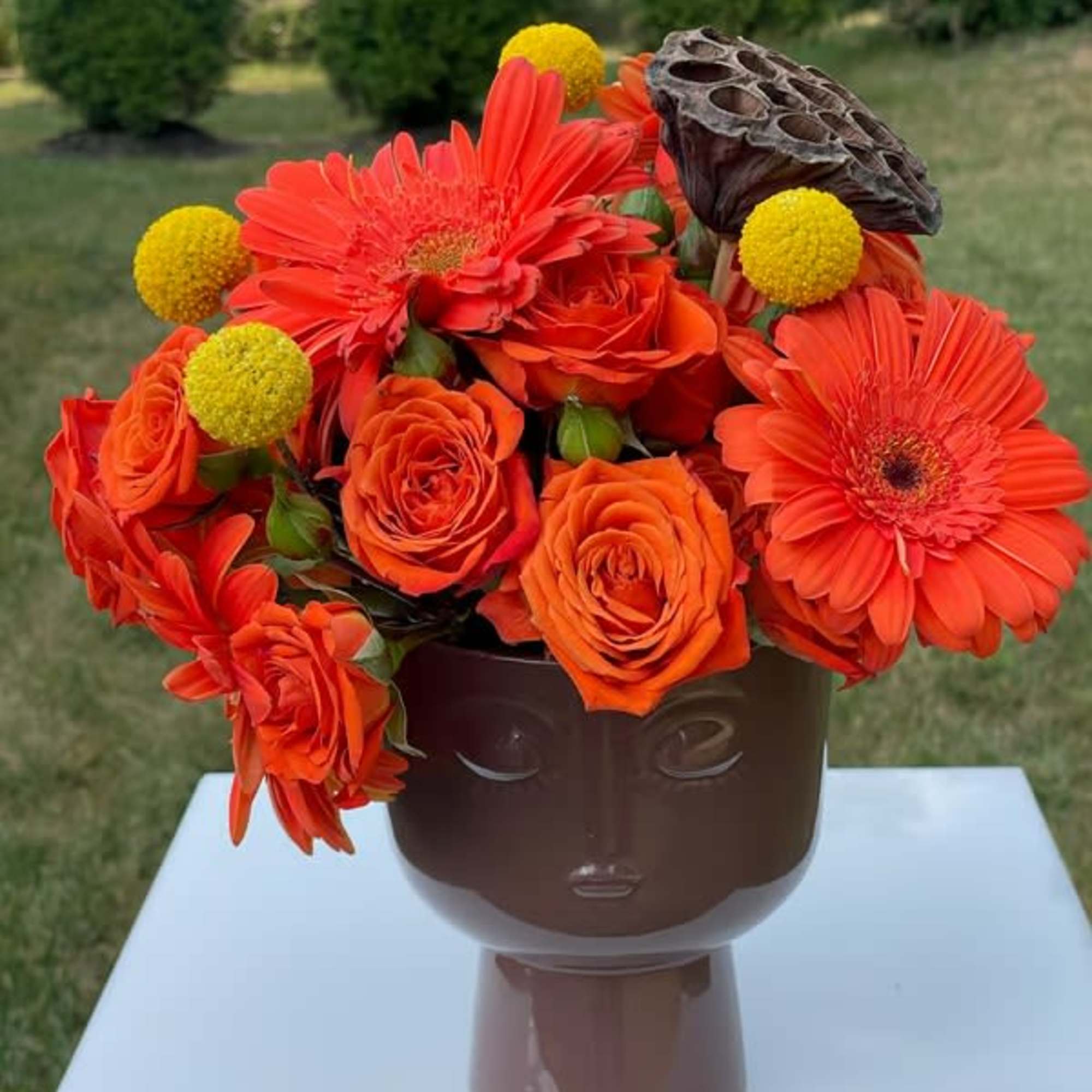 Orange roses and gerbera daisies in a brown face vase