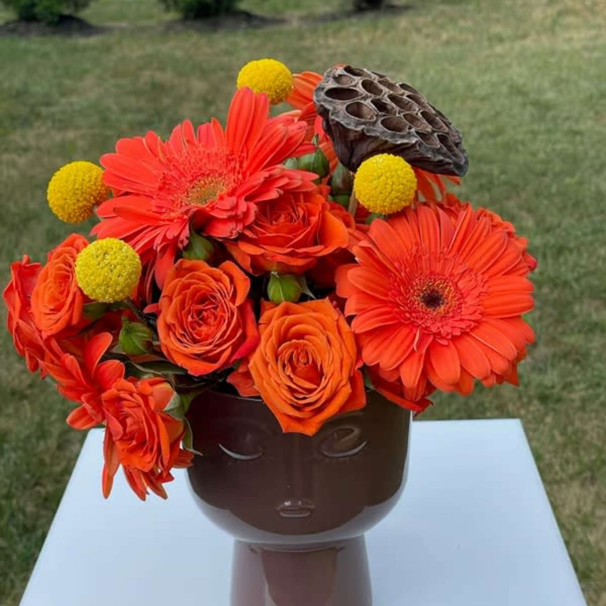 Orange gerbera daisies and roses in a brown vase with yellow pom-pom accents