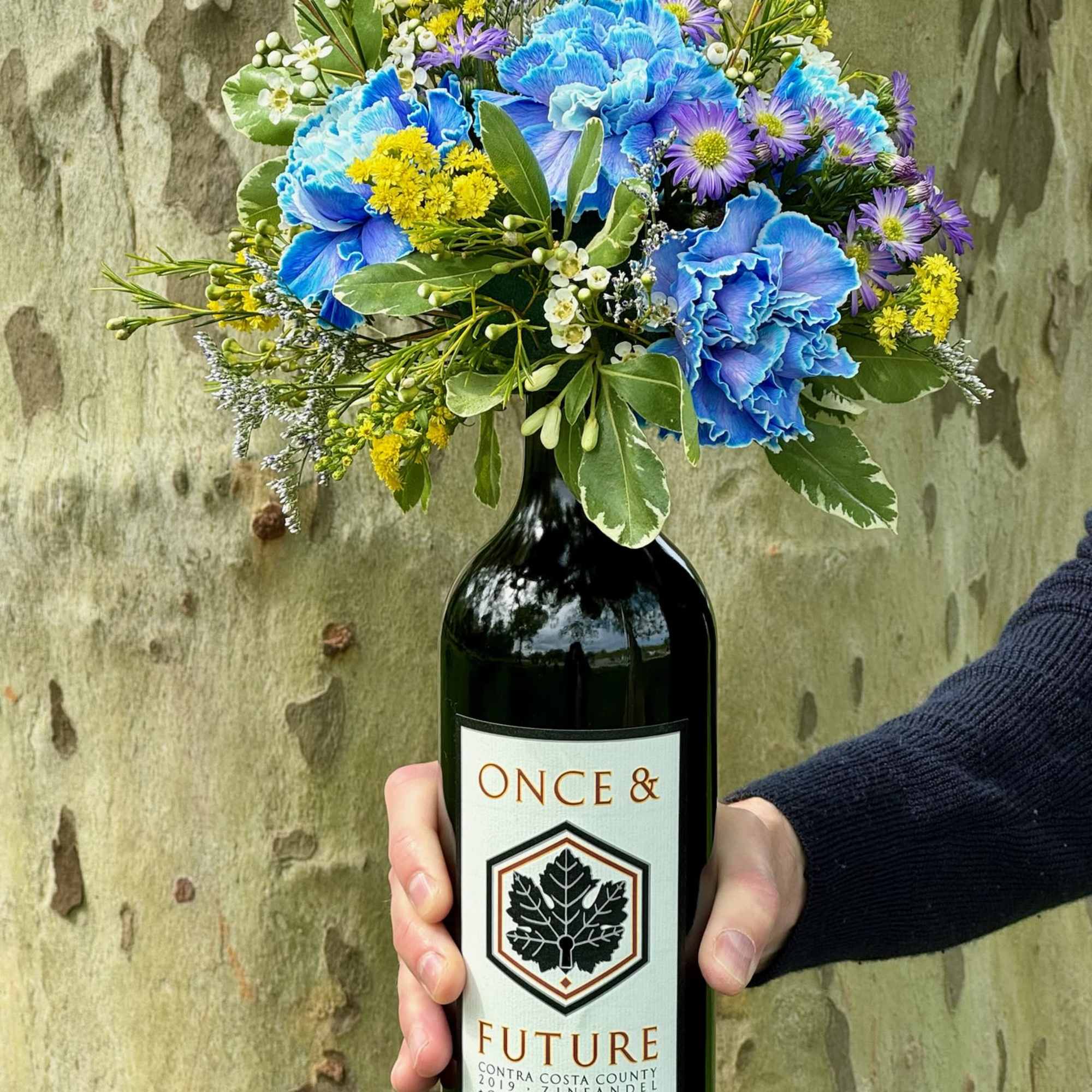 Bouquet of blue, purple, and yellow flowers in a wine bottle vase