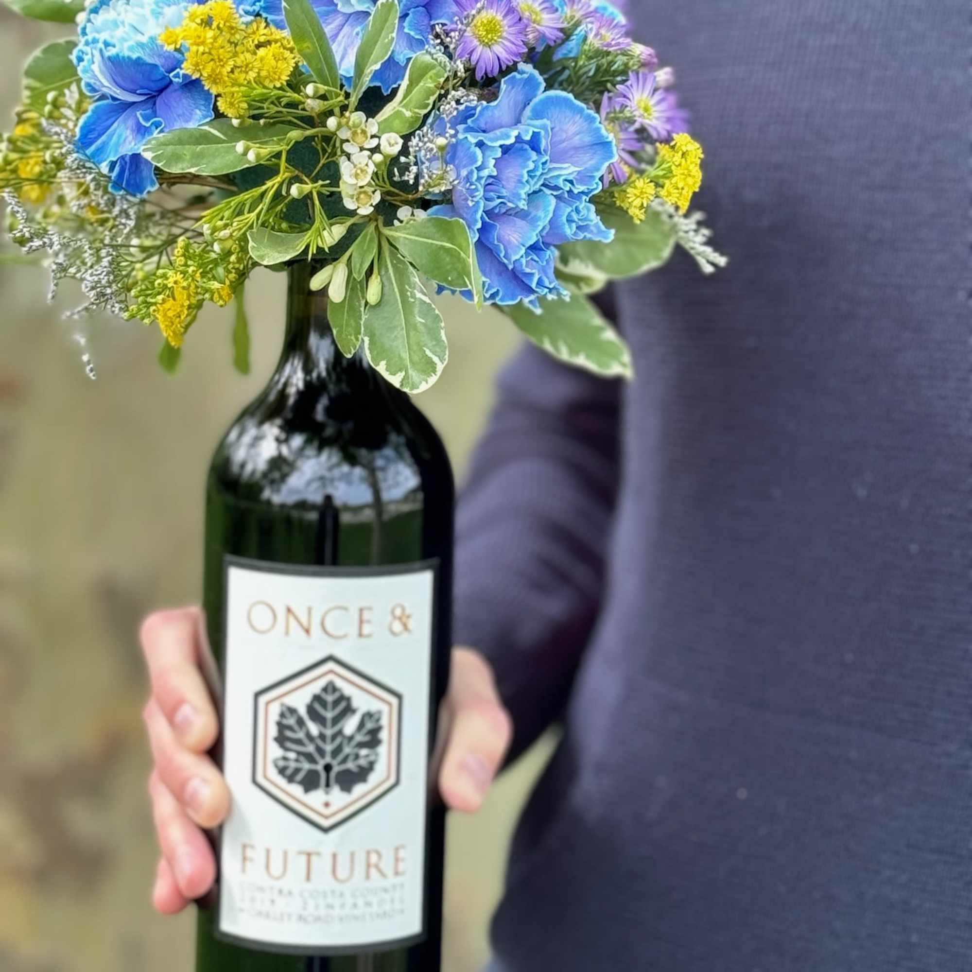 Blue and yellow flower arrangement in a wine bottle vase