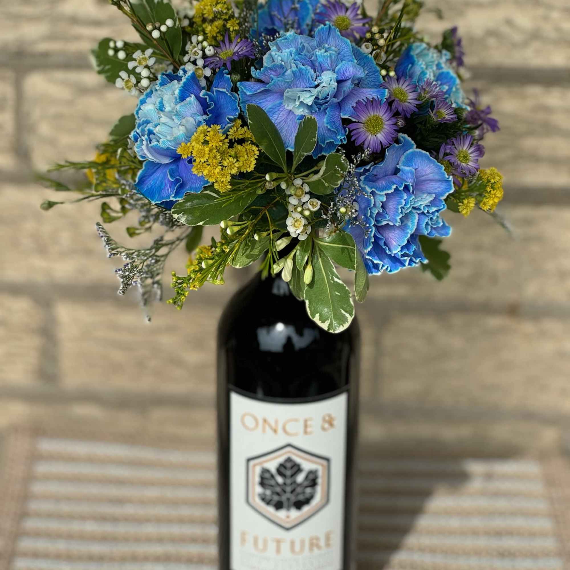 Blue and purple bouquet arranged in a wine bottle vase