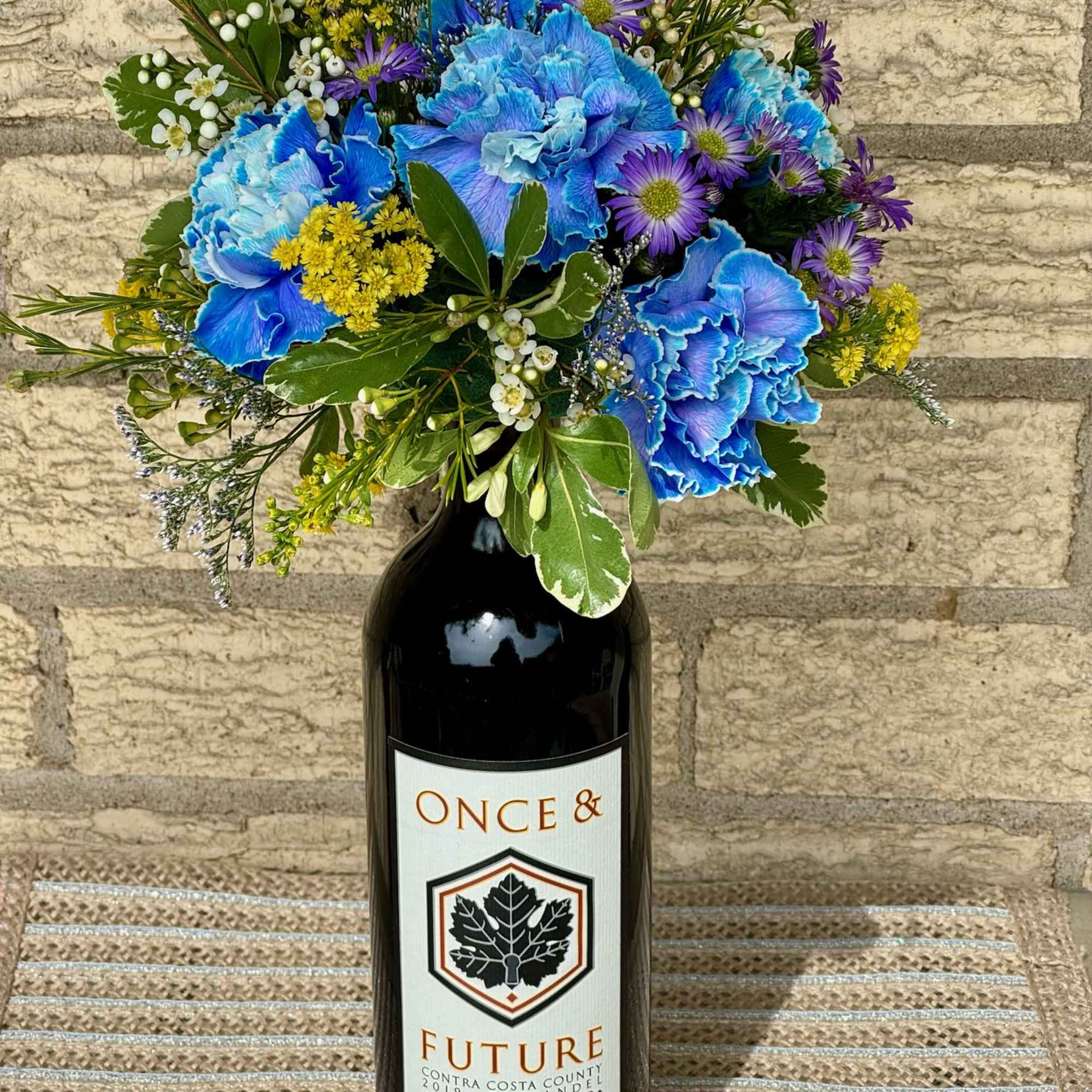 Blue and purple bouquet arranged in a wine bottle vase