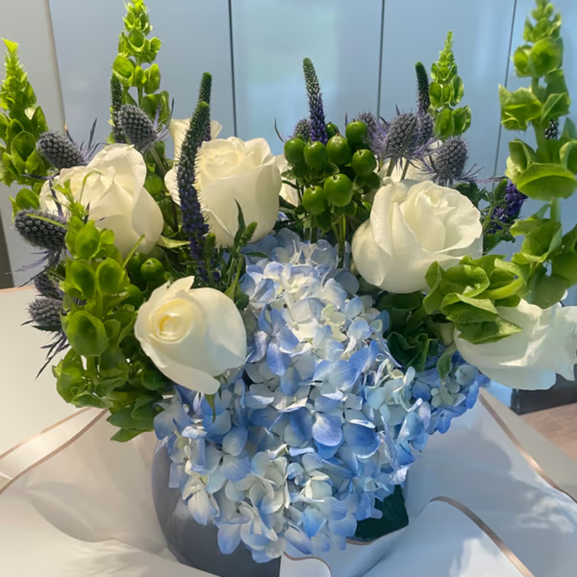 Blue hydrangeas with white roses and green spikes in a wrapped bouquet