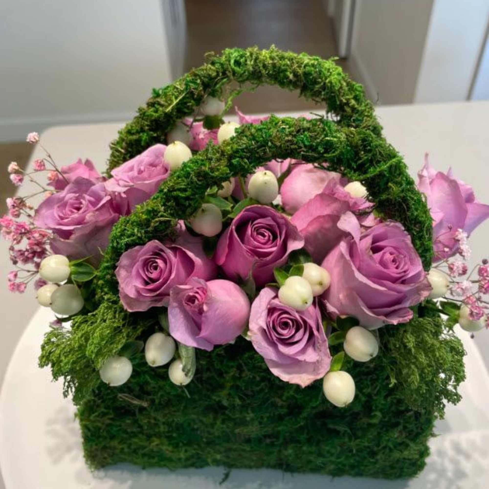 Purple roses in a moss-covered basket with white berries