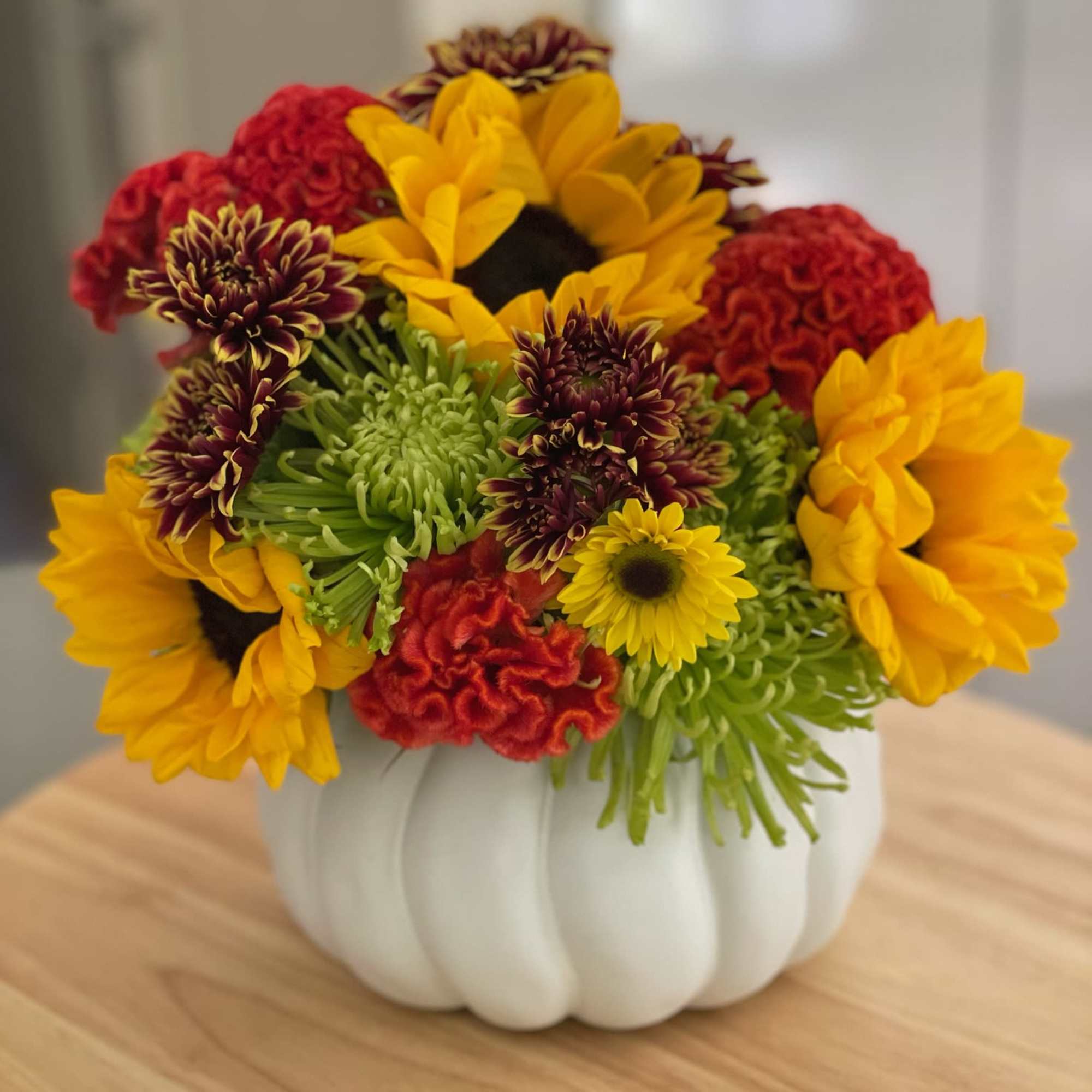 Mixed bouquet of sunflowers, chrysanthemums, and red cockscomb in a white pumpkin vase