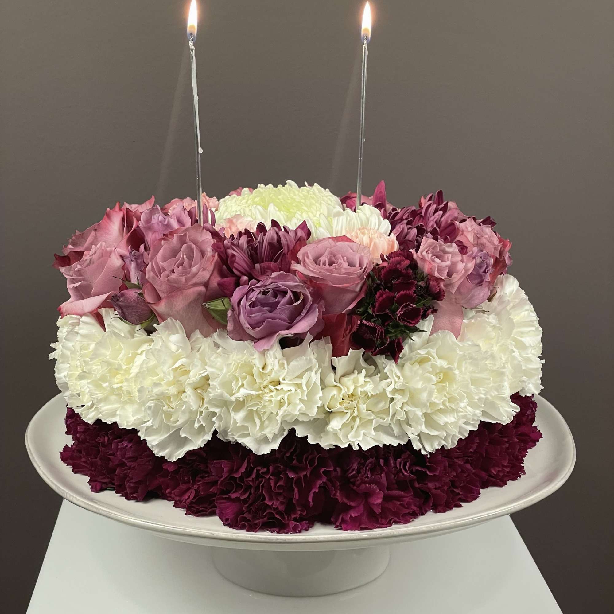 Round floral cake with pink and white flowers and two lit candles