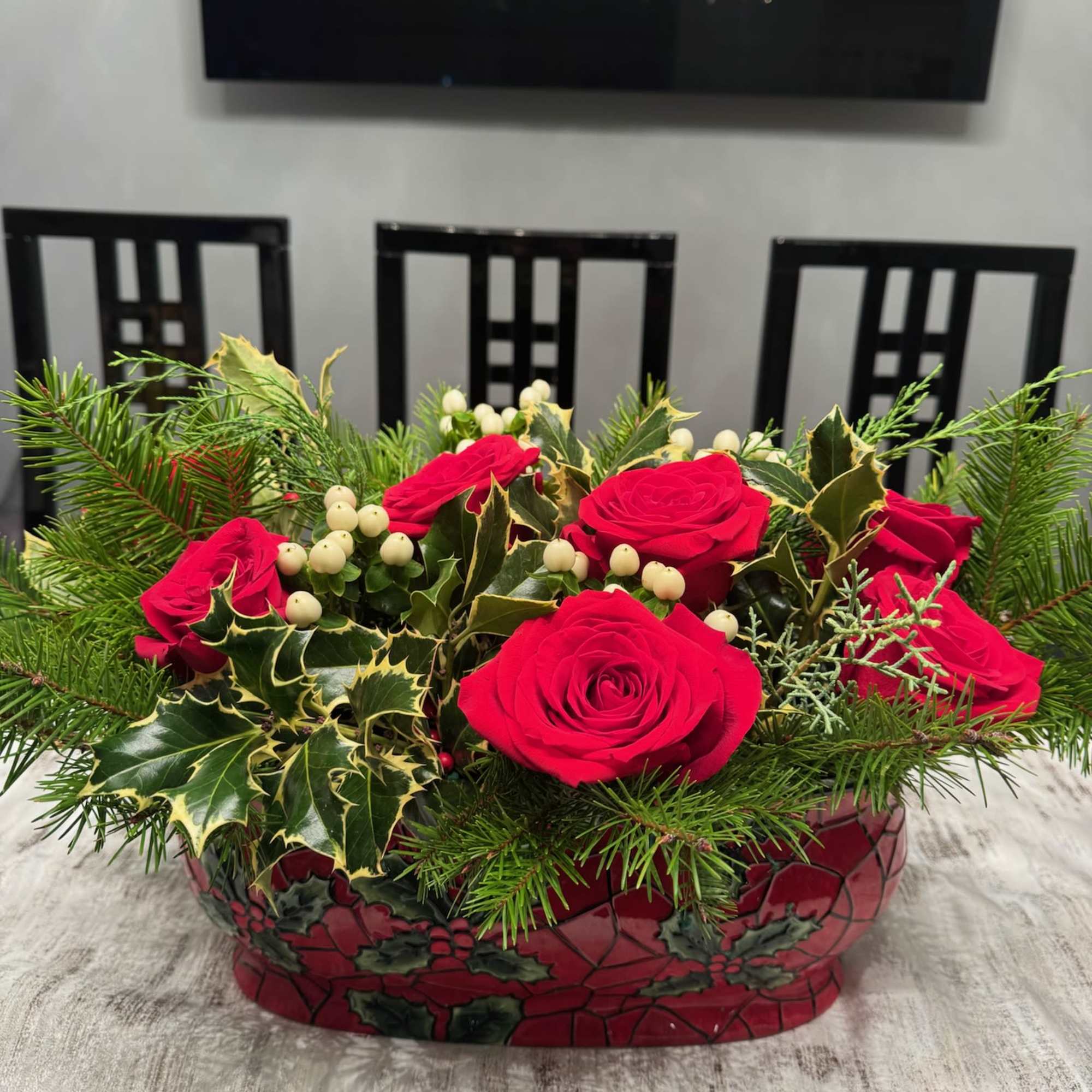 Red roses in a decorative holiday container with evergreen and berry accents