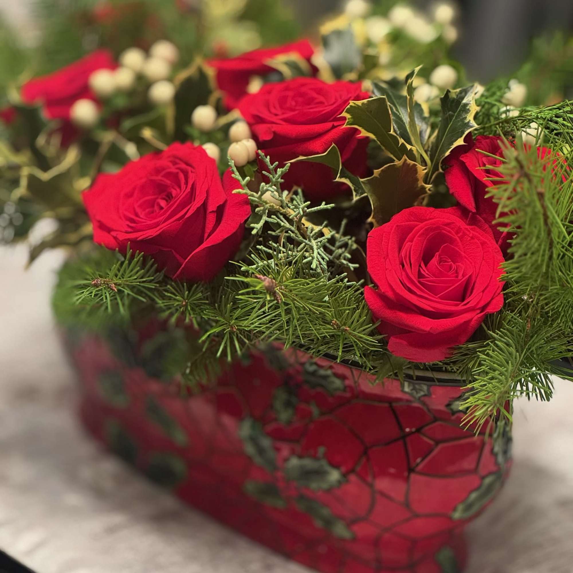 Red roses arranged in a red container with evergreen accents