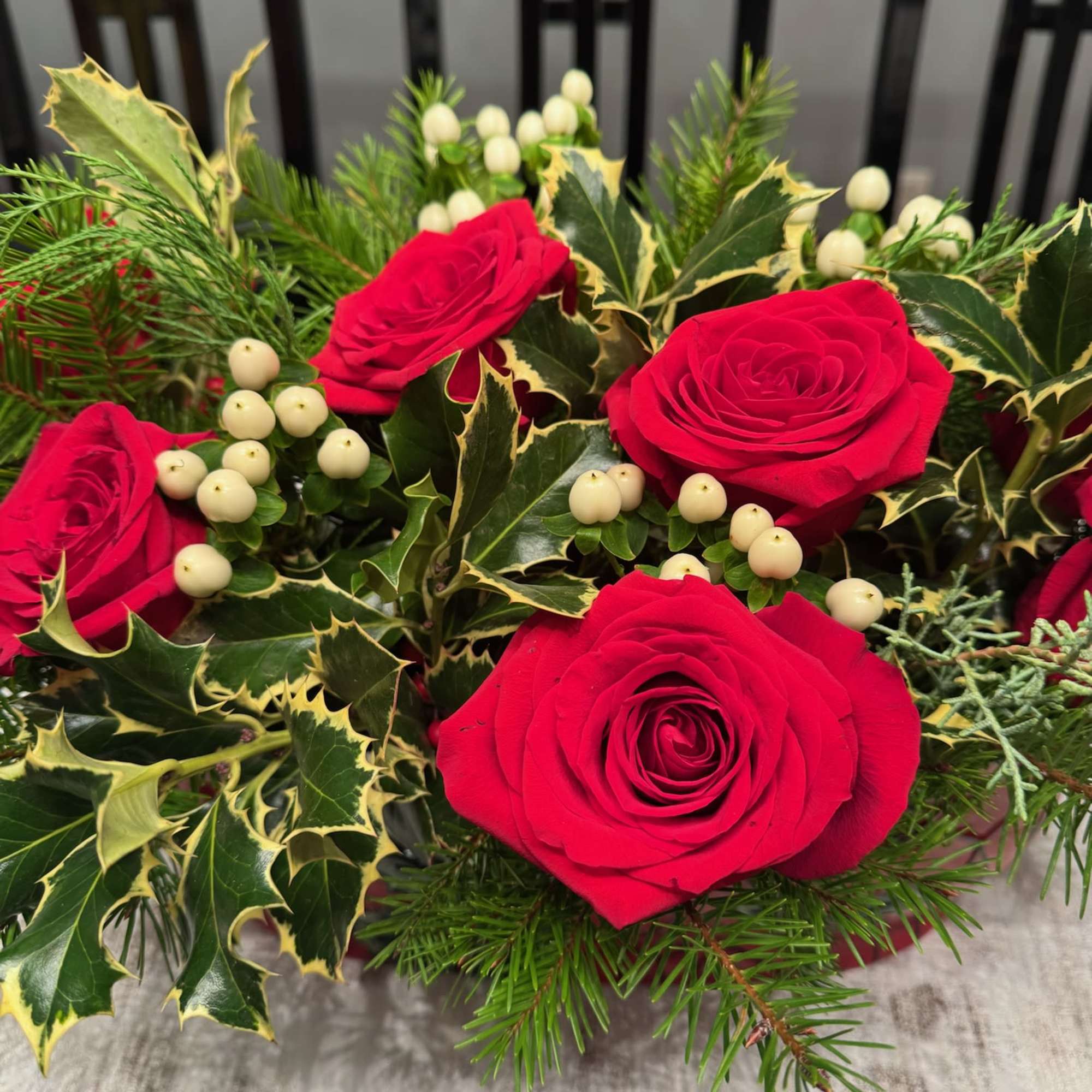 Red roses with holly and white berries in a festive arrangement