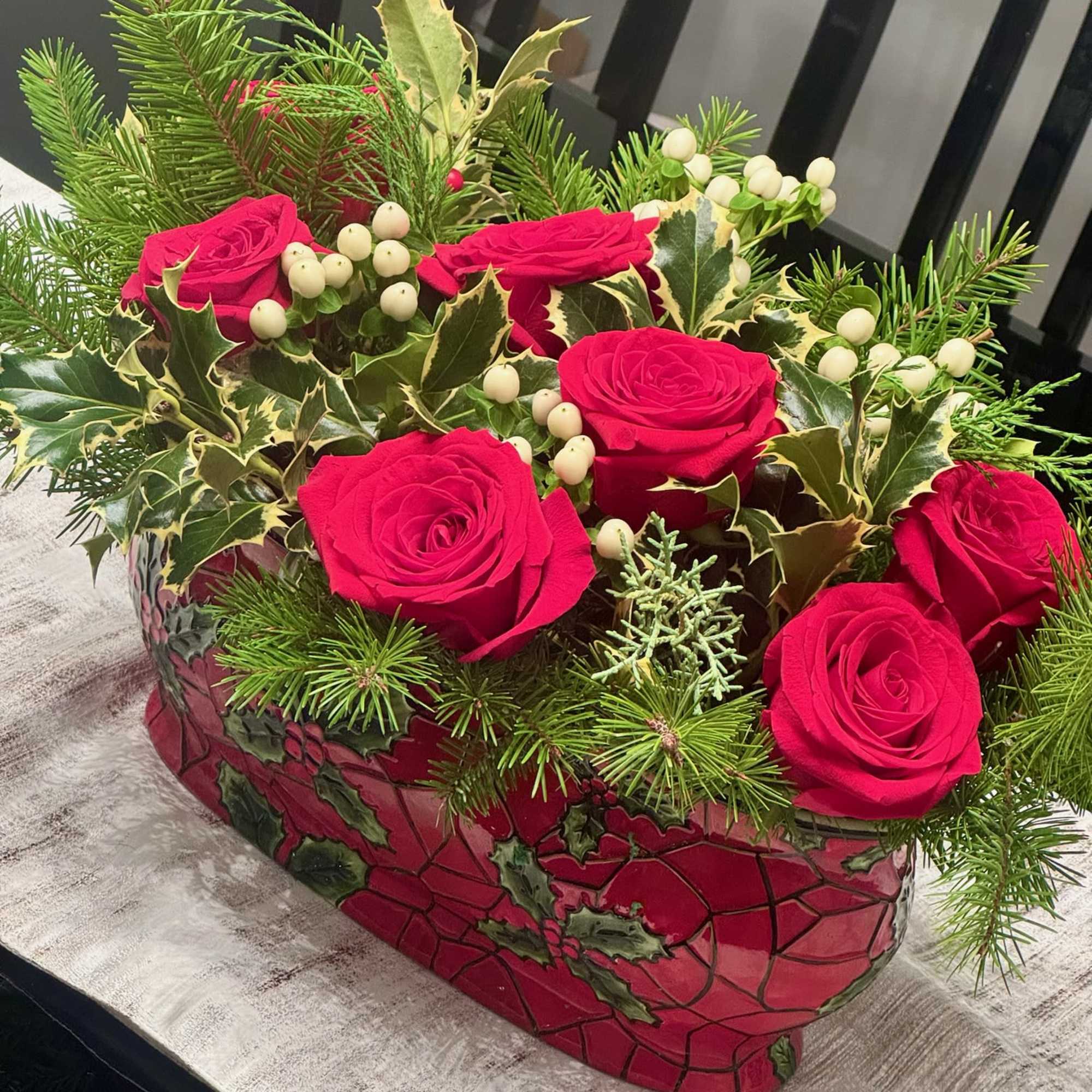Red roses in a decorative holiday container with pine and white berries