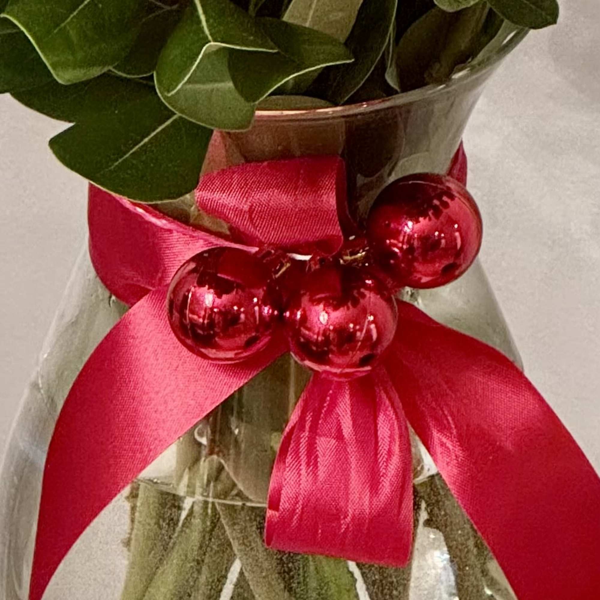 Bouquet in a clear vase with a bright pink ribbon and red ornaments