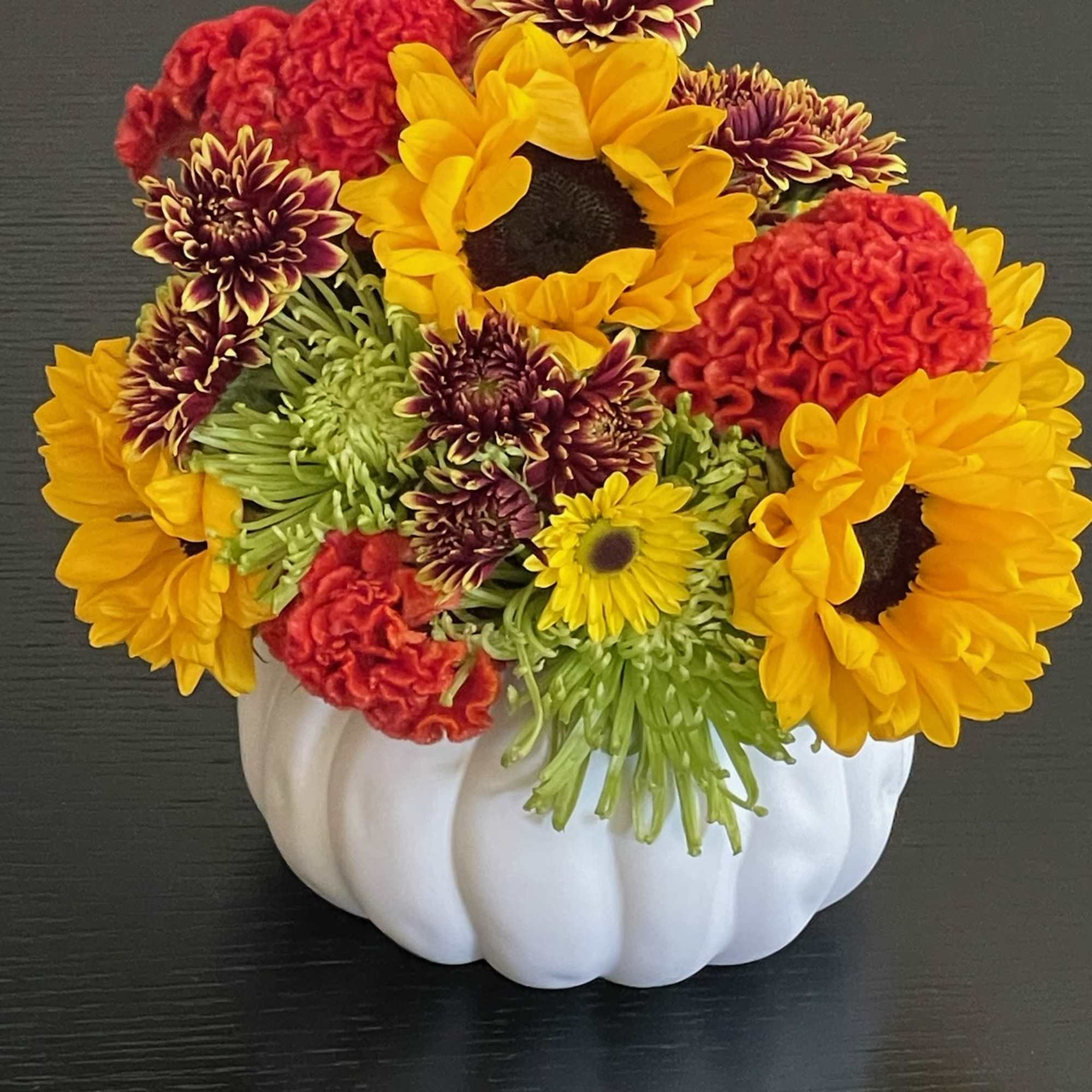 Sunflowers, chrysanthemums, and red carnations in a white pumpkin vase