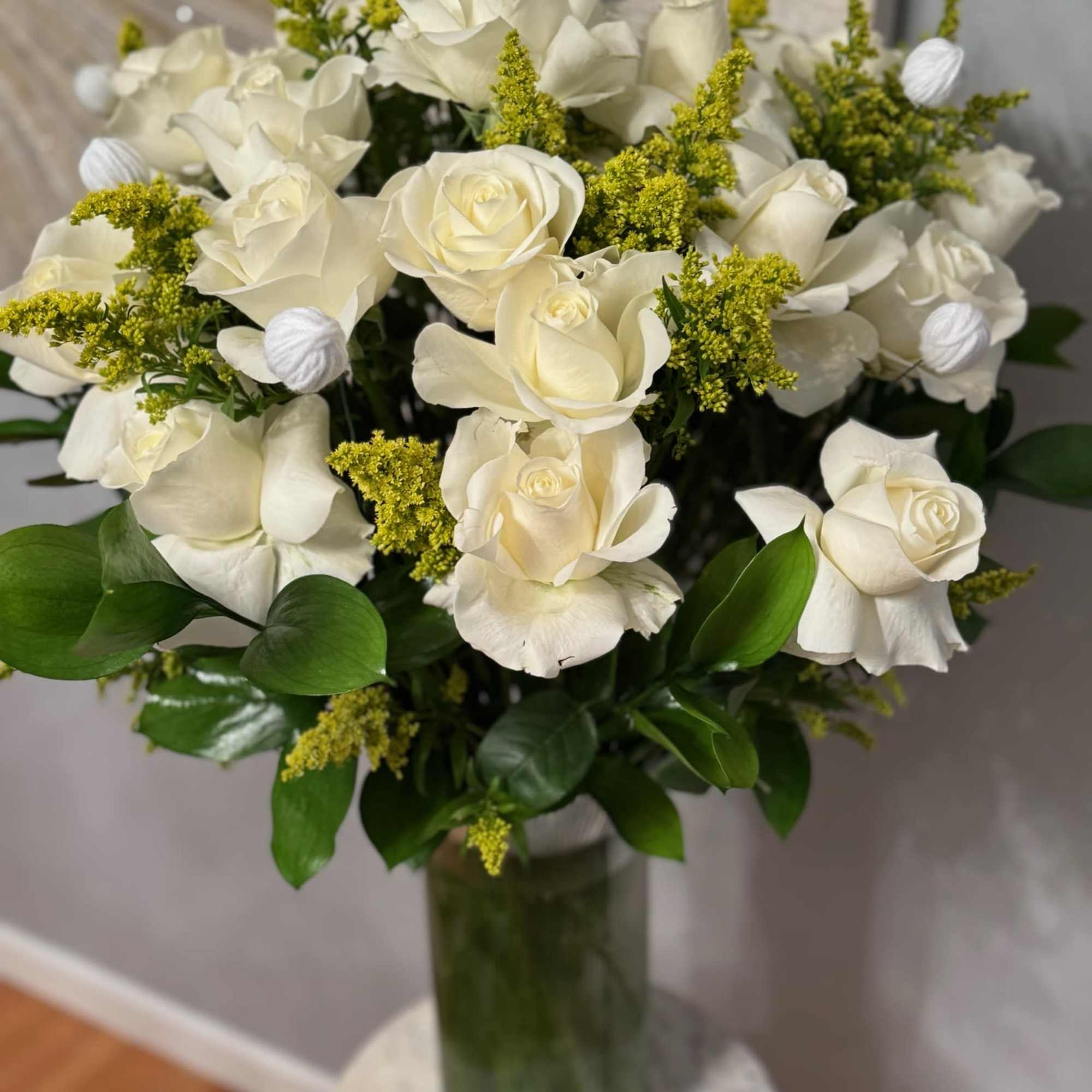 White rose bouquet with yellow filler flowers in a glass vase