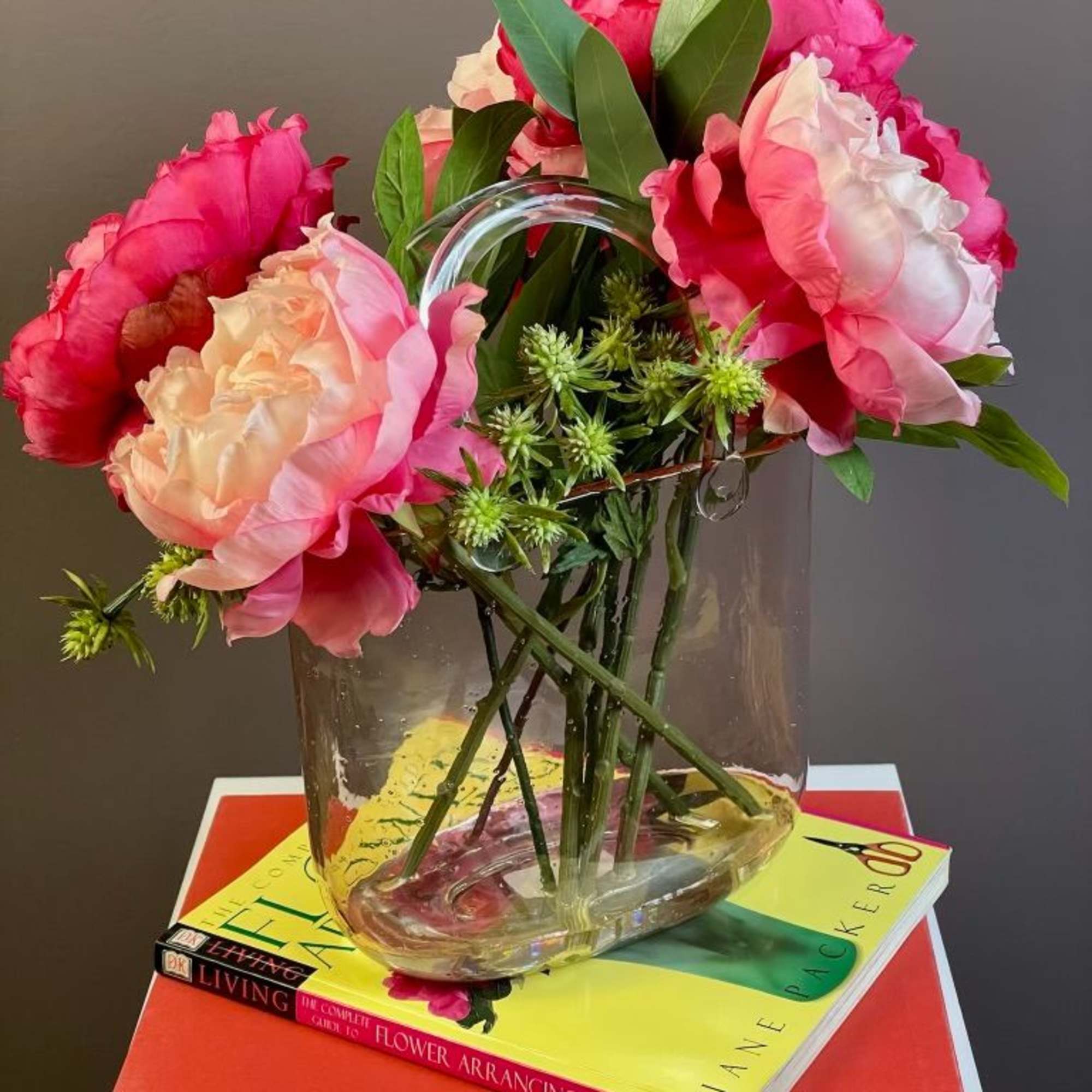 Pink and peach peonies in a clear glass vase on stacked books