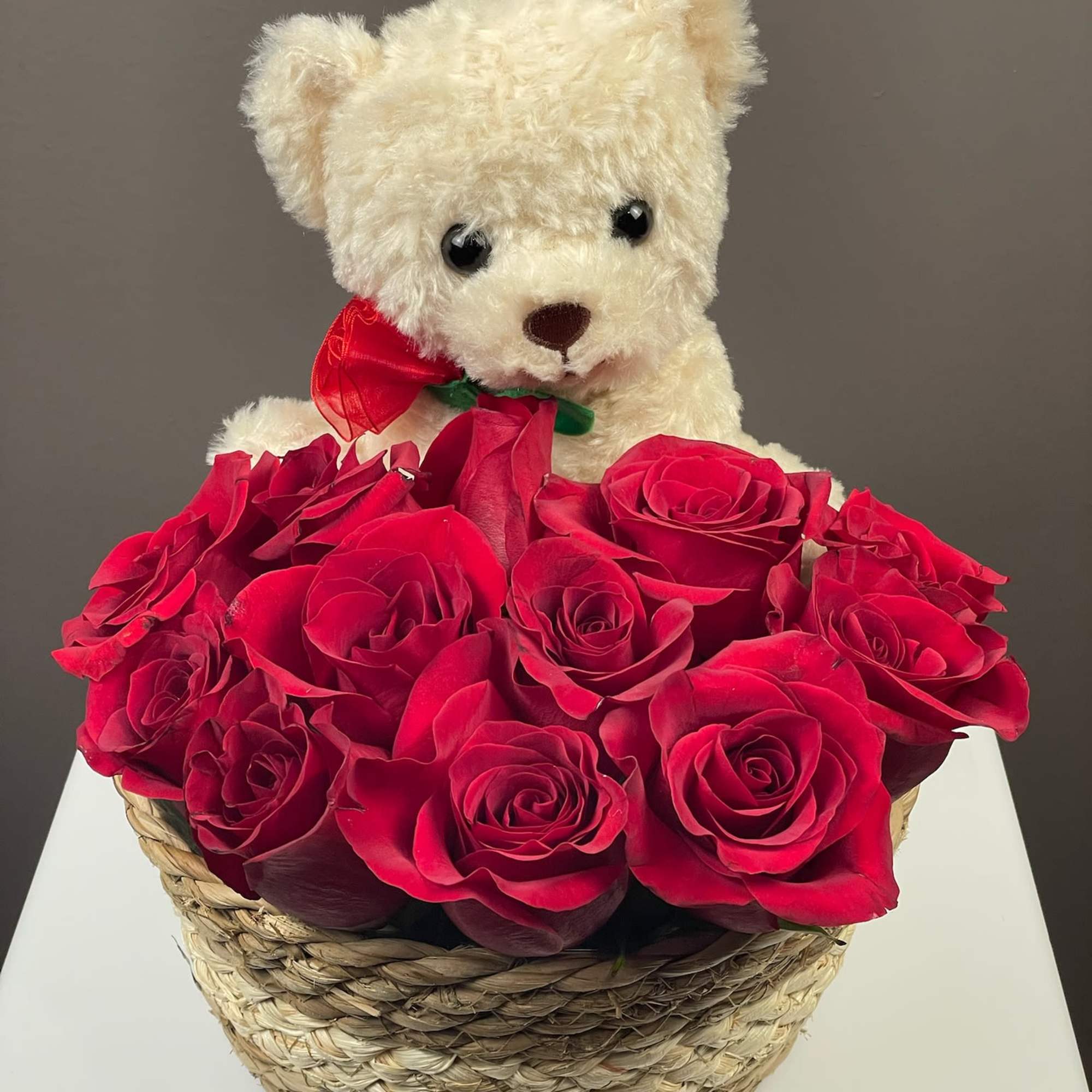 White teddy bear in a basket of red roses