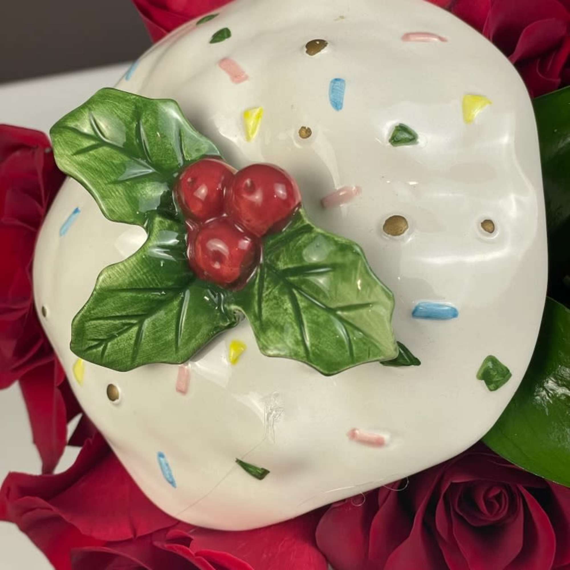 Red roses surrounding a white ceramic ornament with holly decoration