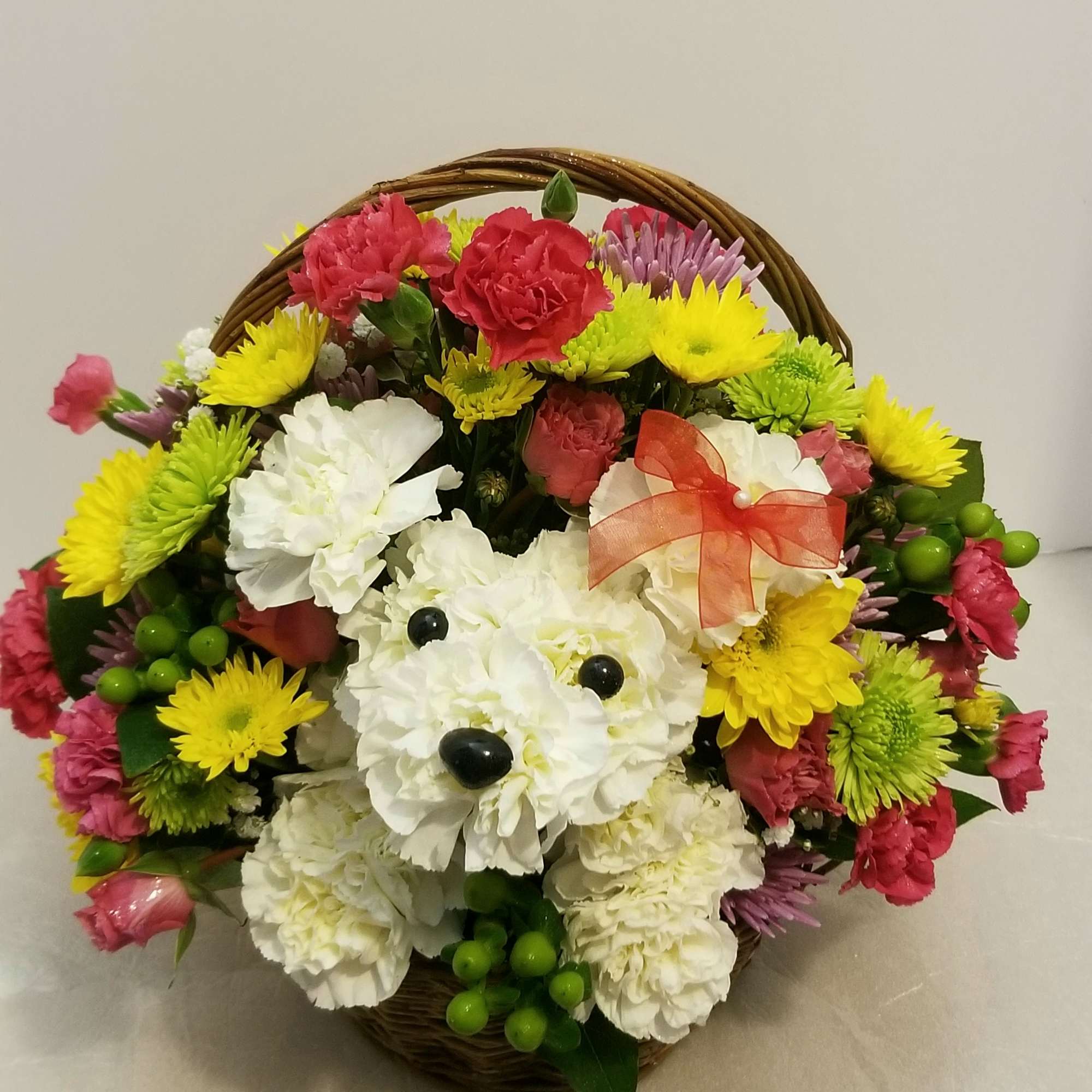 Basket arrangement of white, pink, yellow, and green flowers with a ribbon bow