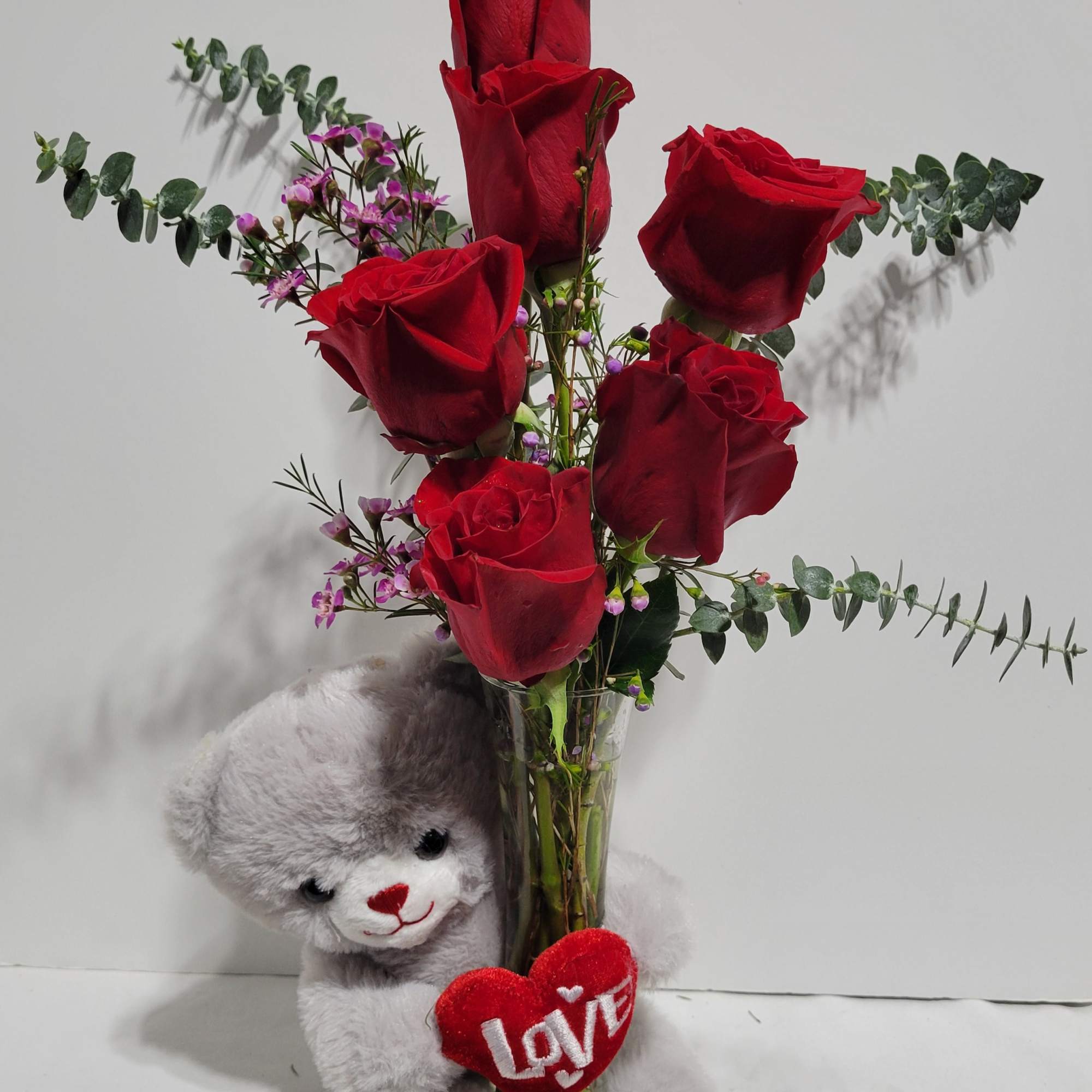 Red roses in a glass vase with a teddy bear and heart decoration