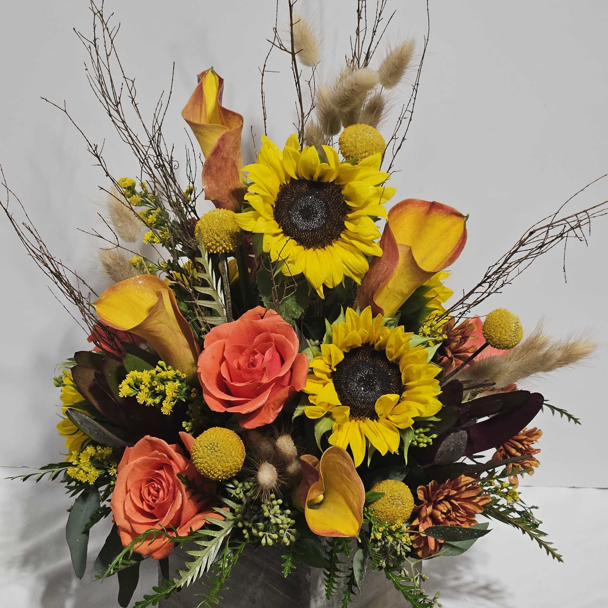 Mixed floral arrangement with sunflowers, orange roses, and calla lilies in a square vase