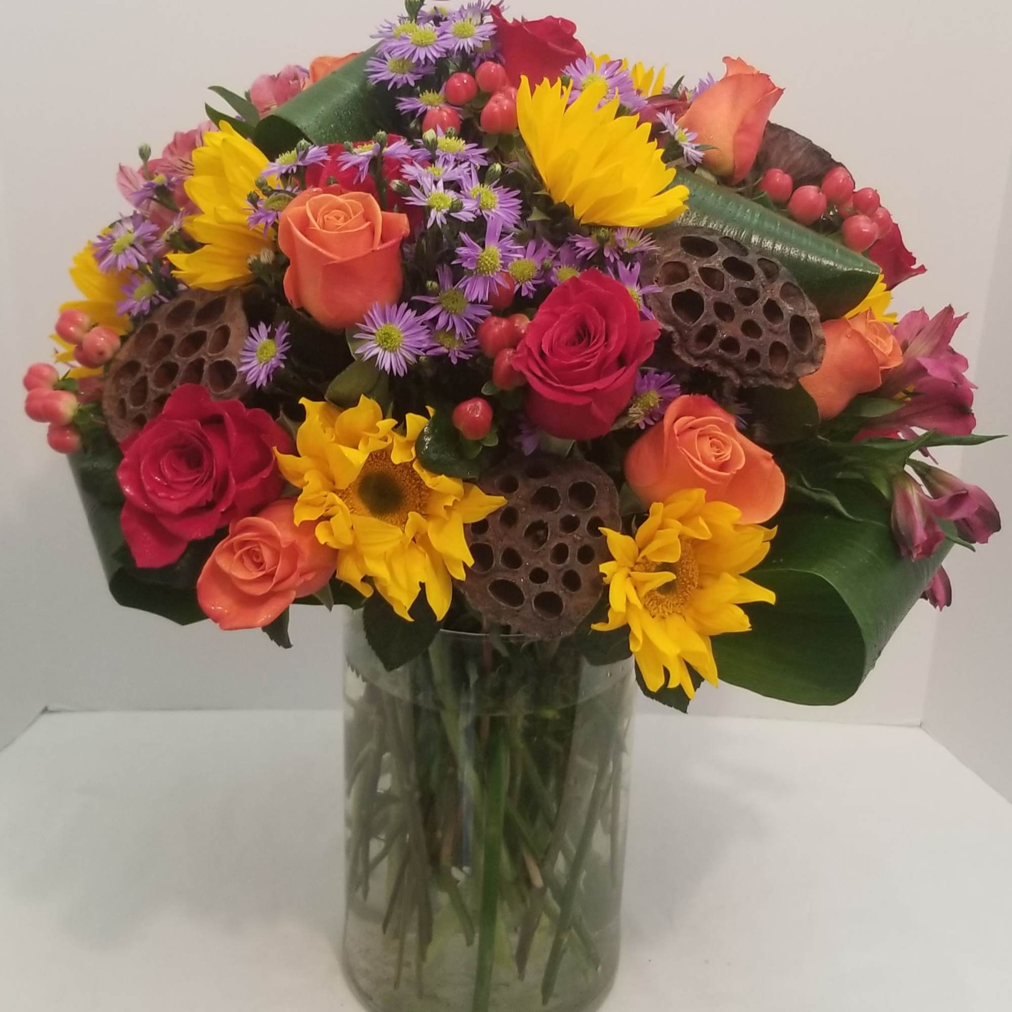 Mixed bouquet of roses, sunflowers, and purple daisies in a glass vase, photo 2 of 2