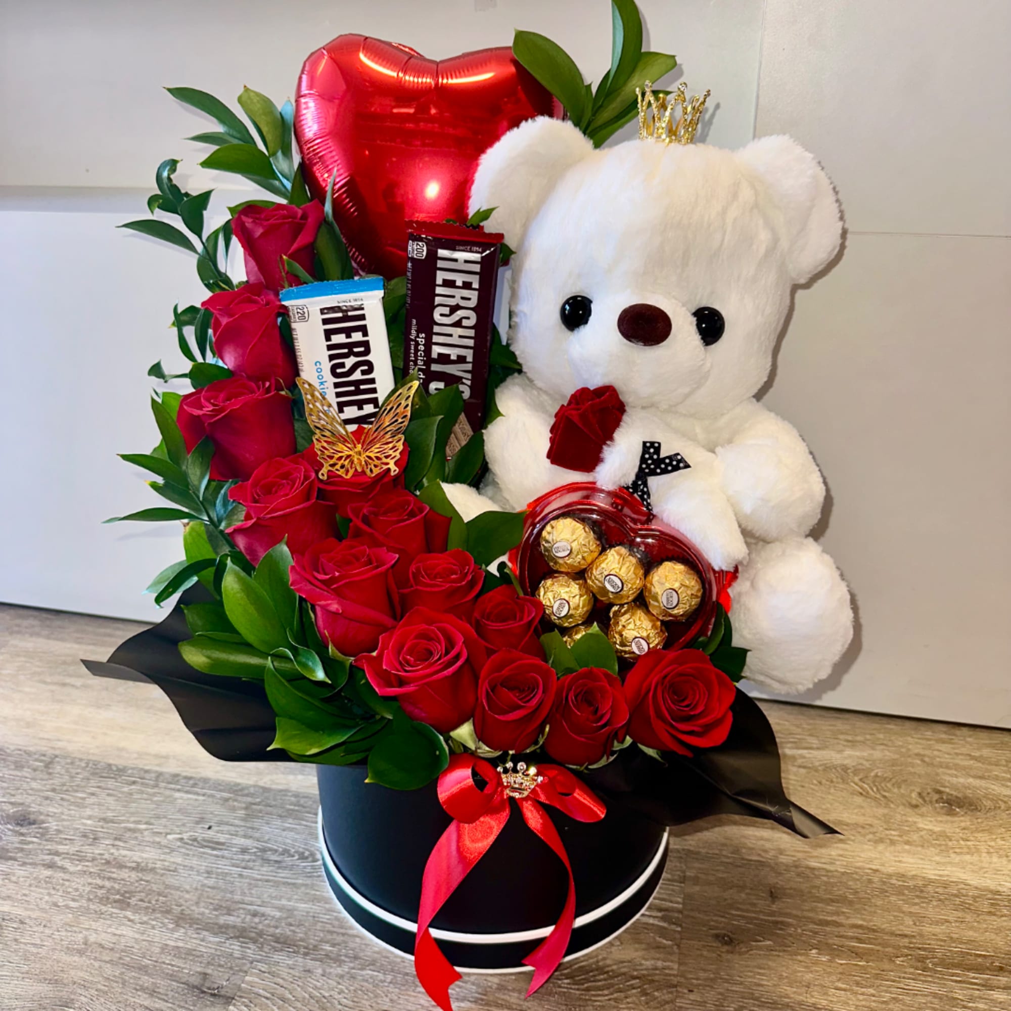 Red roses with chocolates and a white teddy bear in a black hatbox