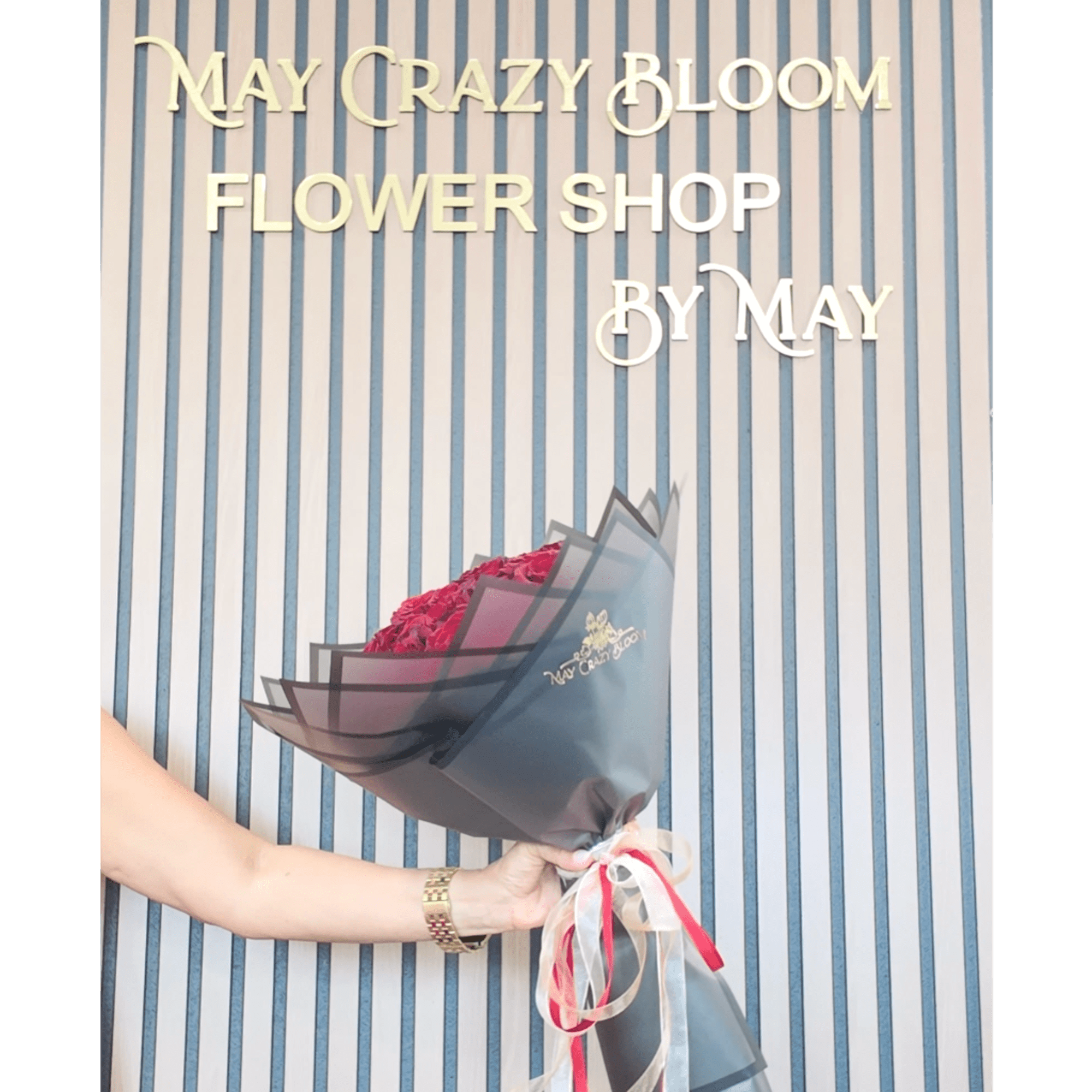 Hand holding a wrapped bouquet of pink roses in front of a flower shop sign