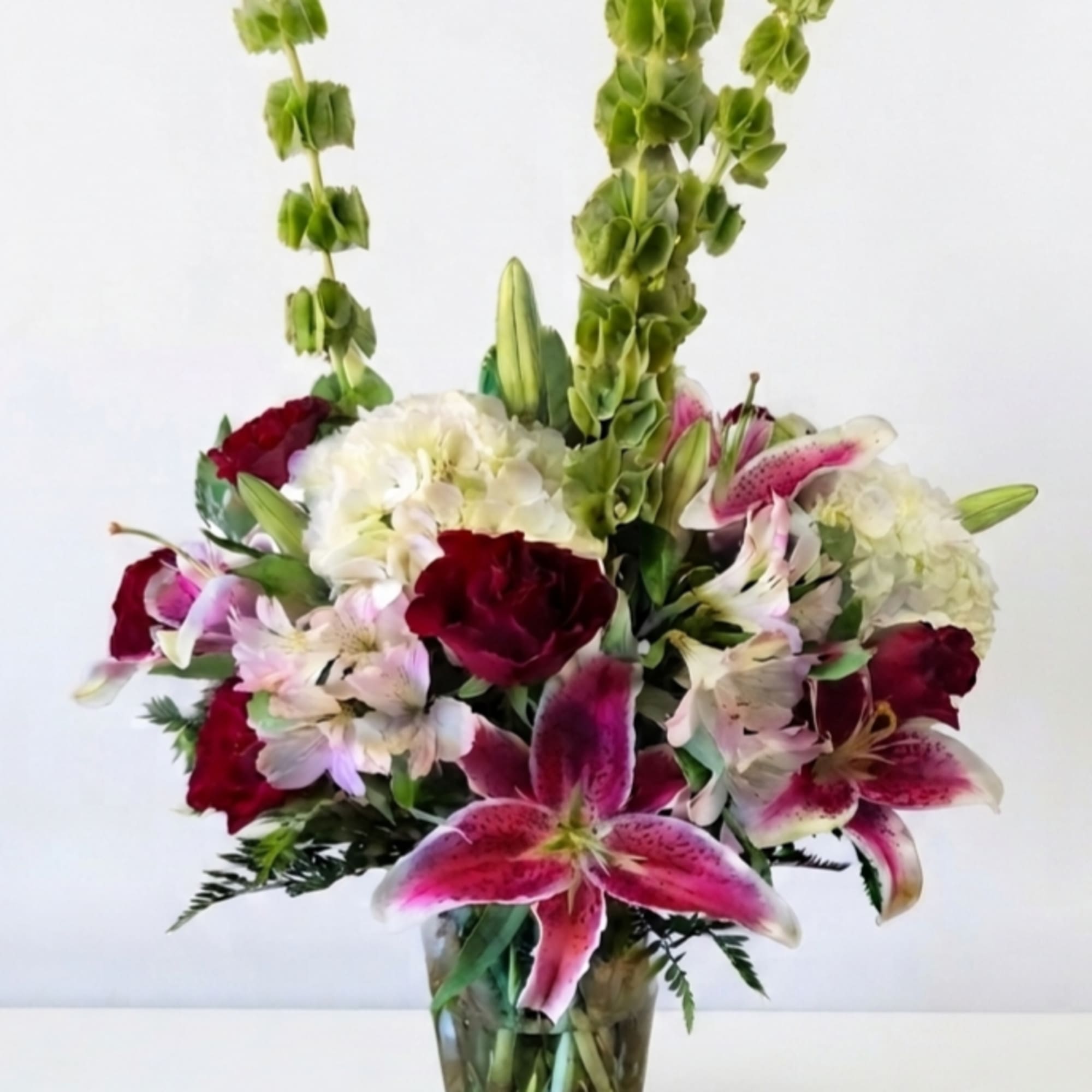 Mixed bouquet of lilies, hydrangeas, and red blooms in a glass vase