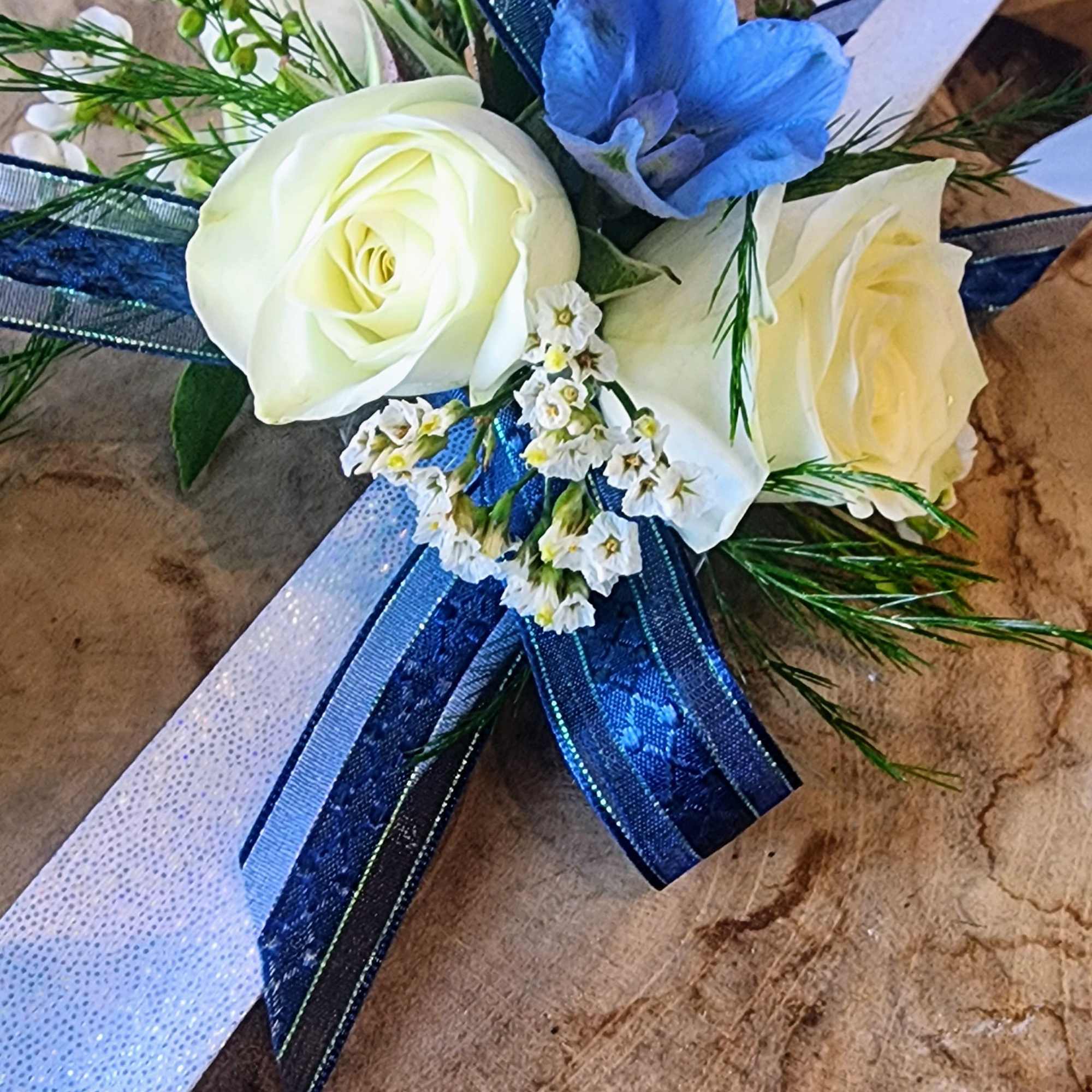 White roses with a blue flower and ribbon accents