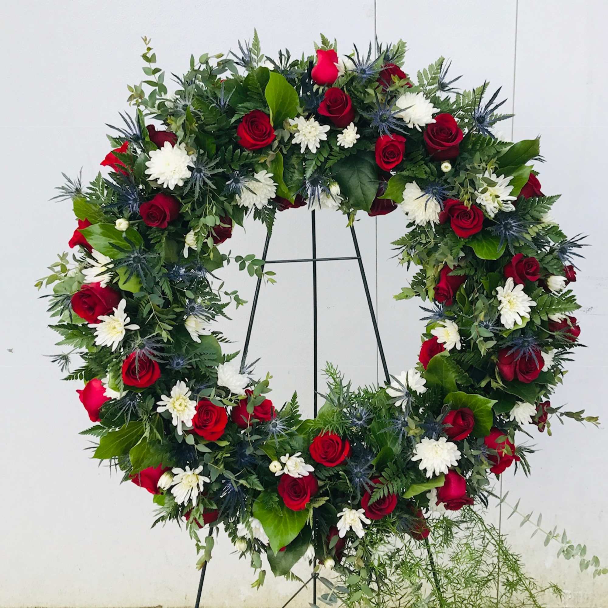 Large floral wreath of red roses and white daisies on a stand