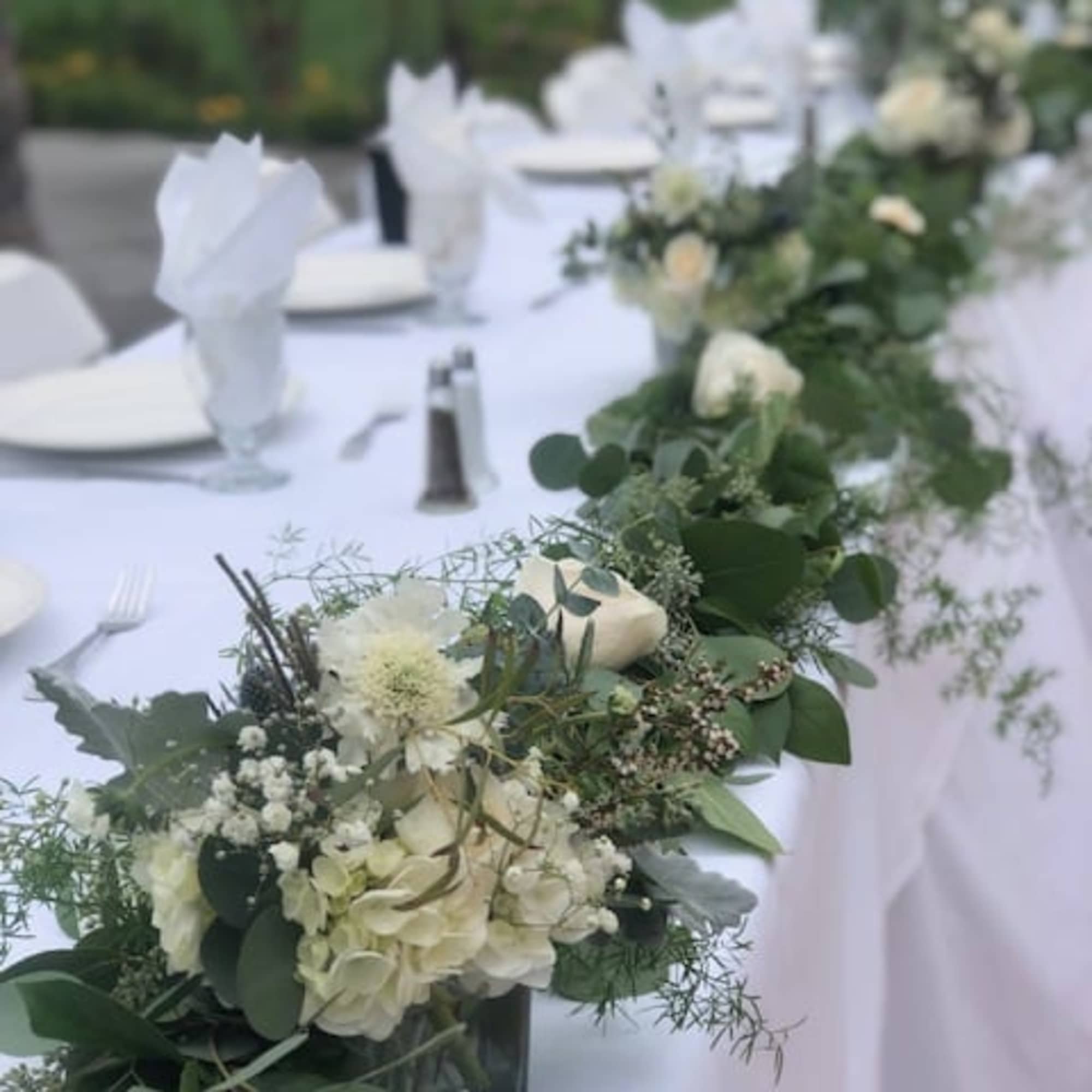 White floral centerpieces line a long table with white linens.