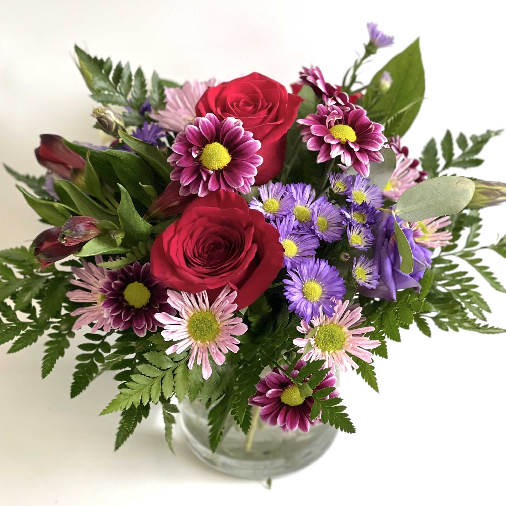 Bouquet of red roses and purple daisies in a clear glass vase