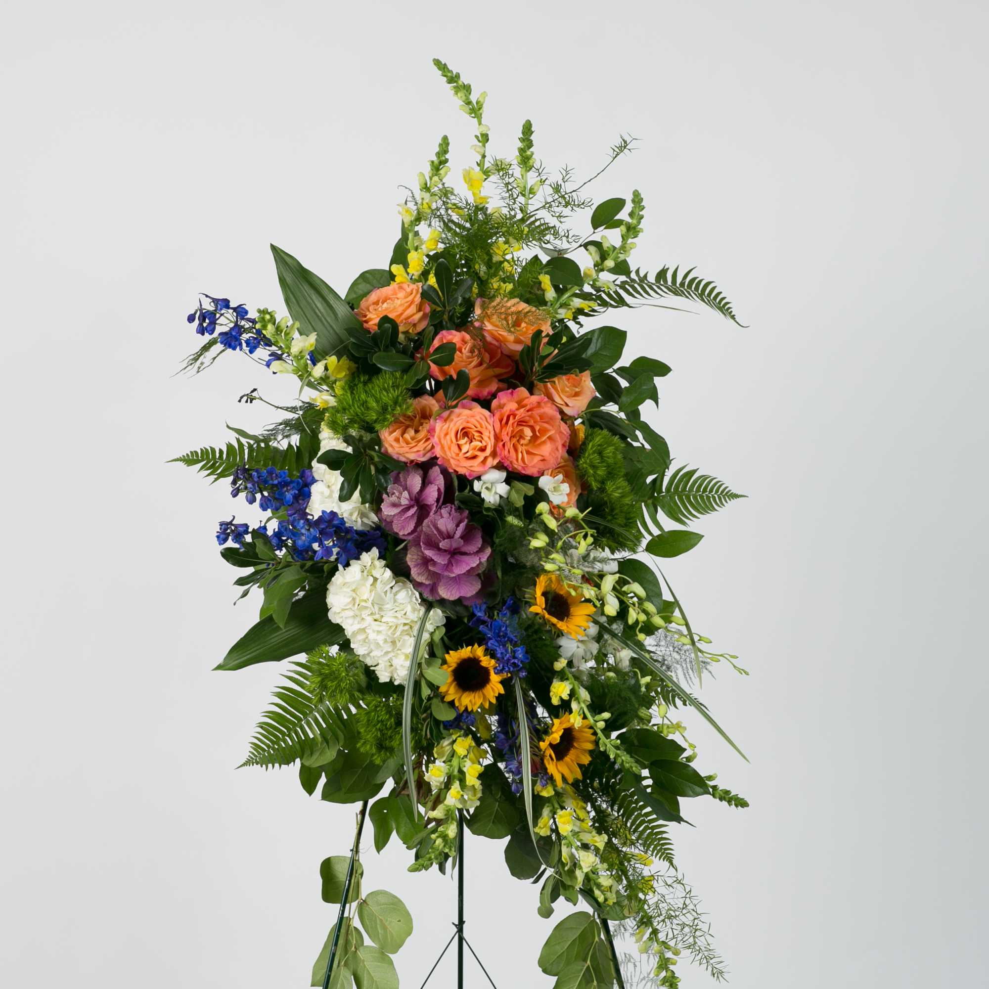 Tall standing floral spray with mixed blooms in peach, blue, yellow, white, and purple