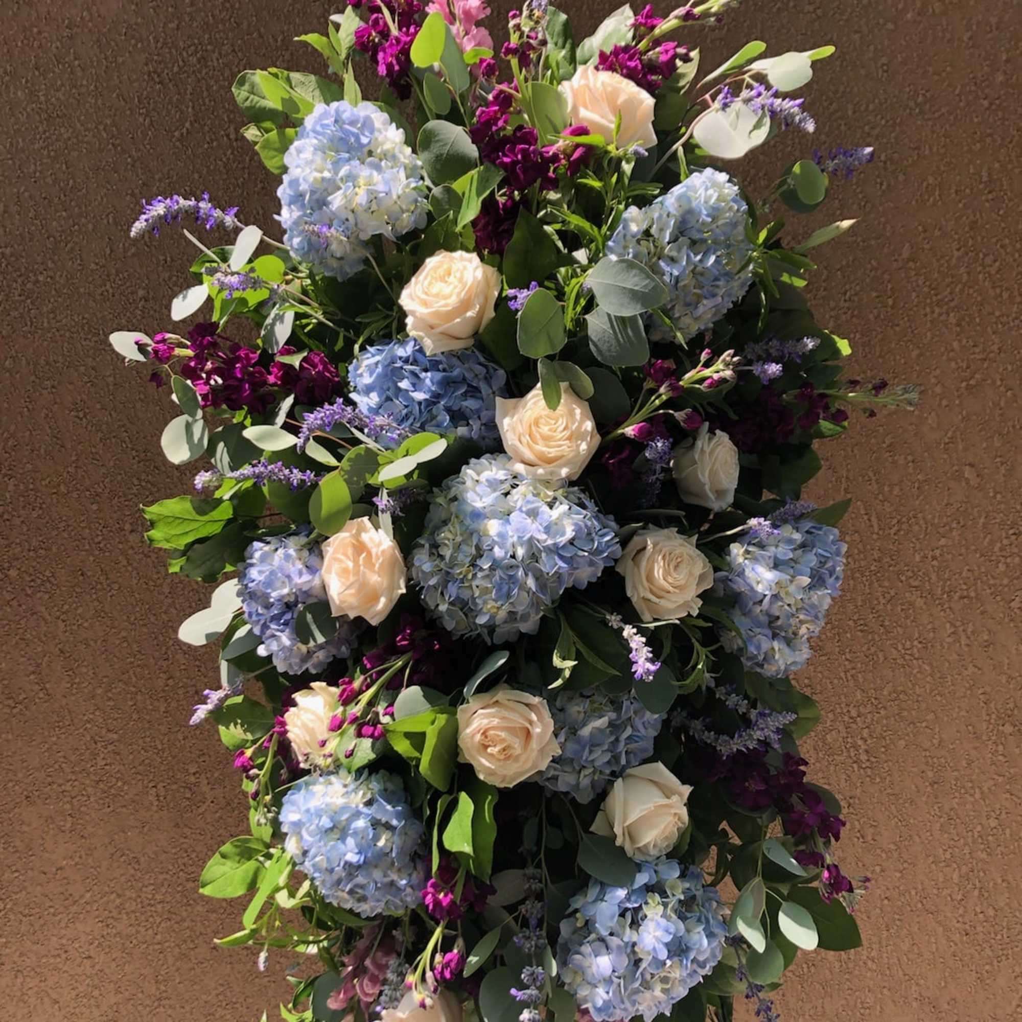 Tall floral spray with blue hydrangeas, cream roses, and purple accents