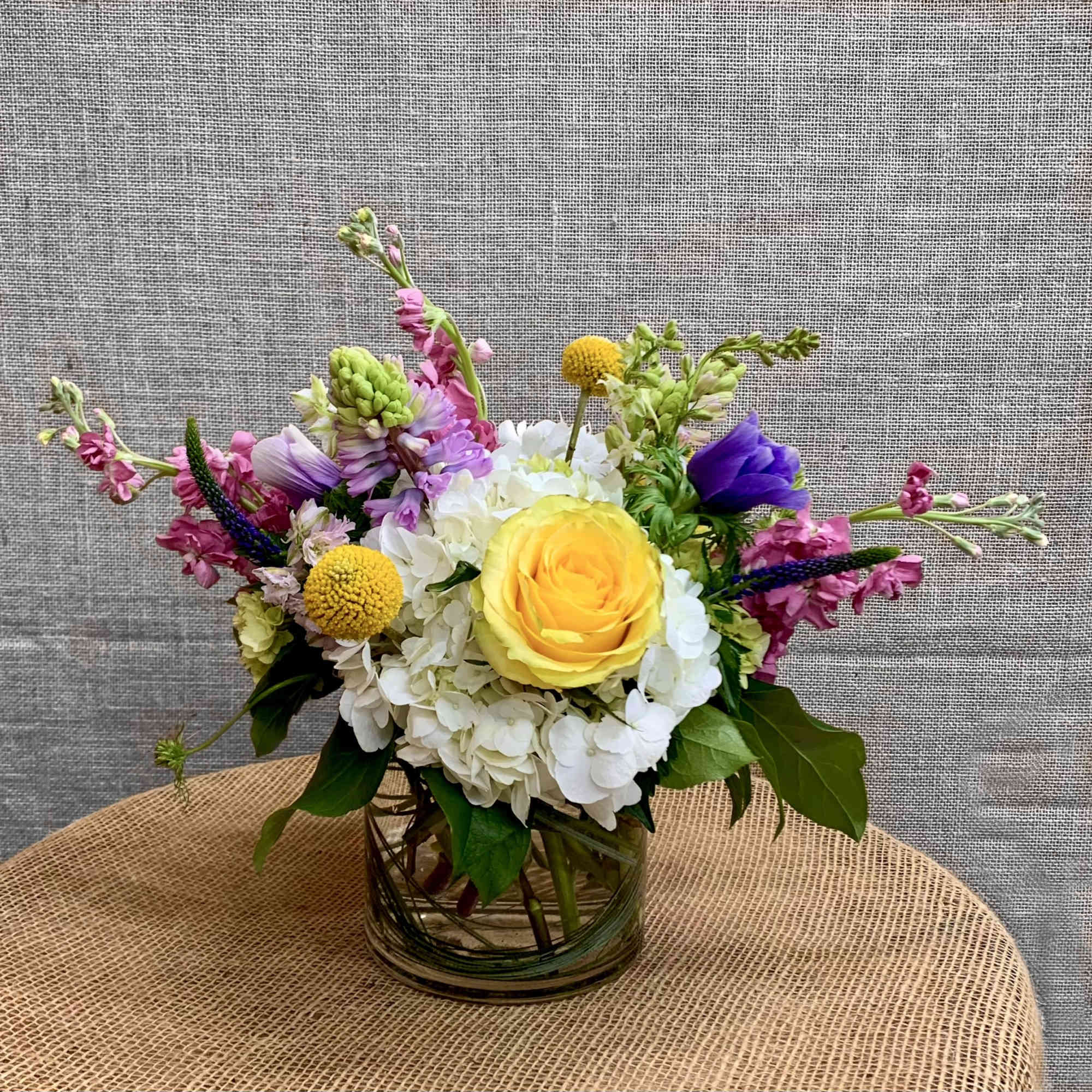 Colorful mixed bouquet in a glass vase with a yellow rose and white hydrangea