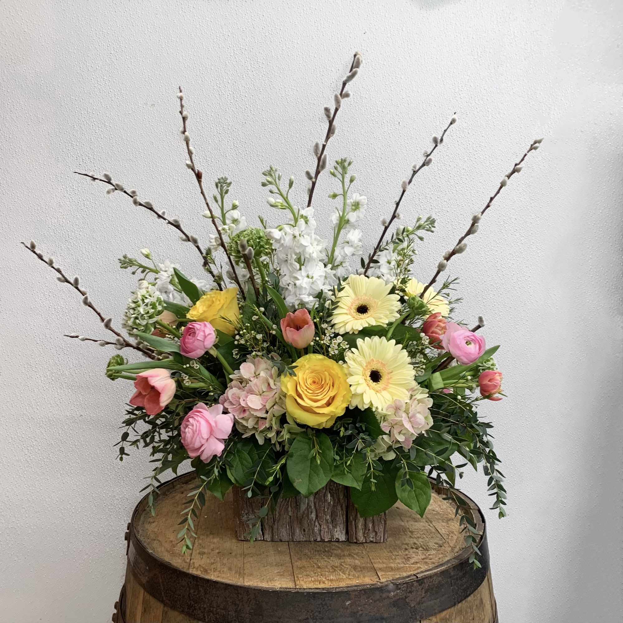 Mixed bouquet with yellow roses, pink blooms, and white flowers in a rustic wooden container