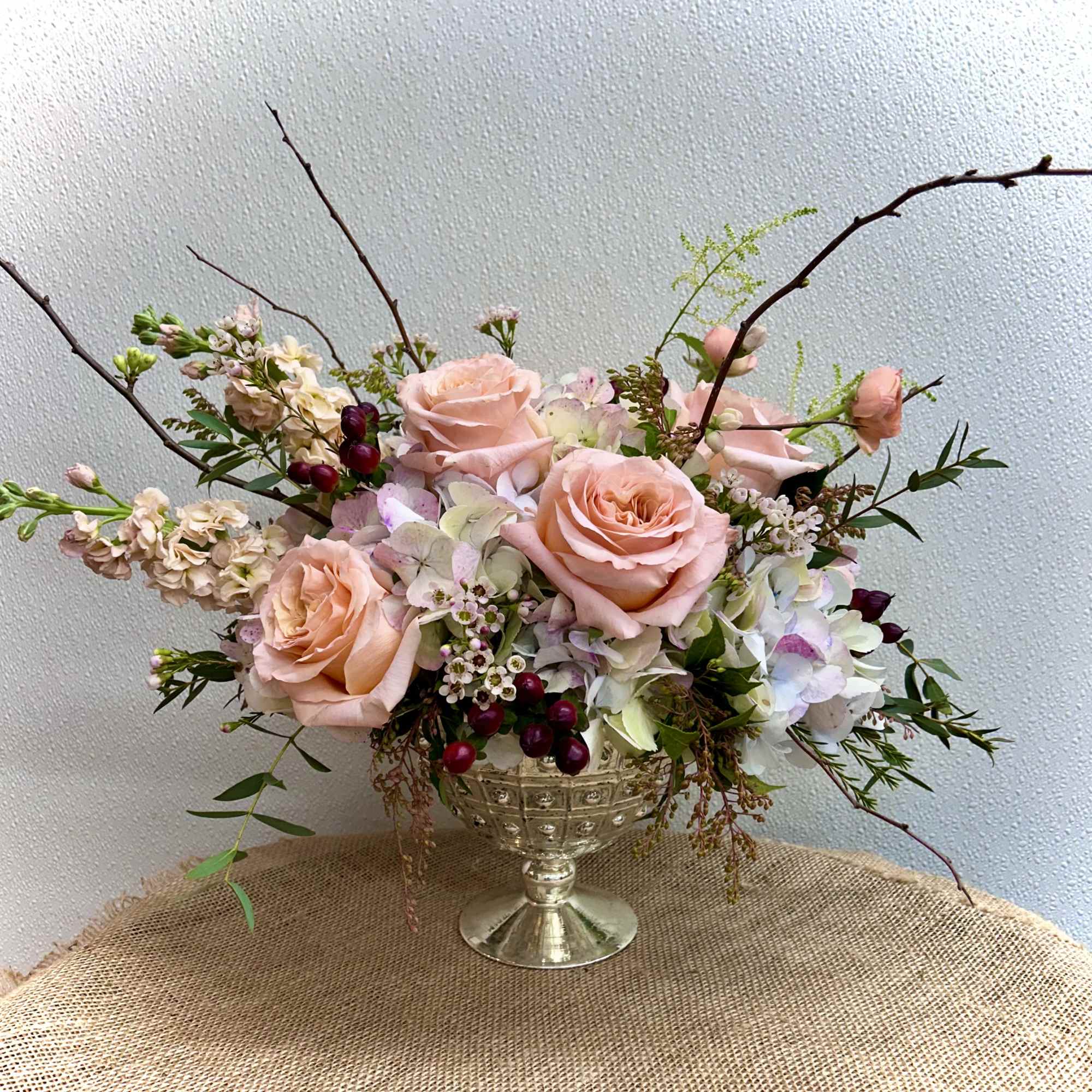 Peach roses and pale hydrangeas arranged in a silver pedestal vase
