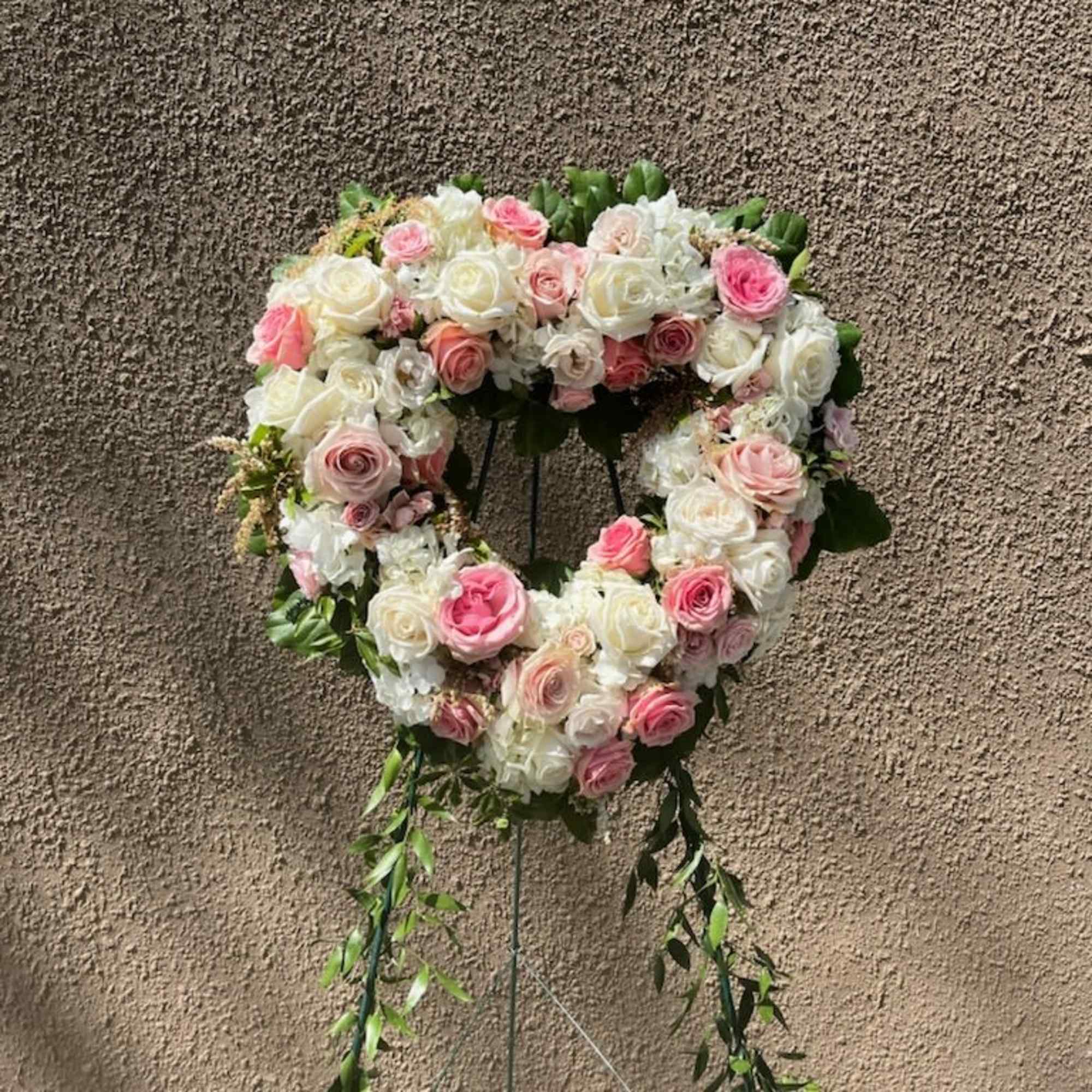 Heart-shaped floral wreath of pink and white roses on a stand