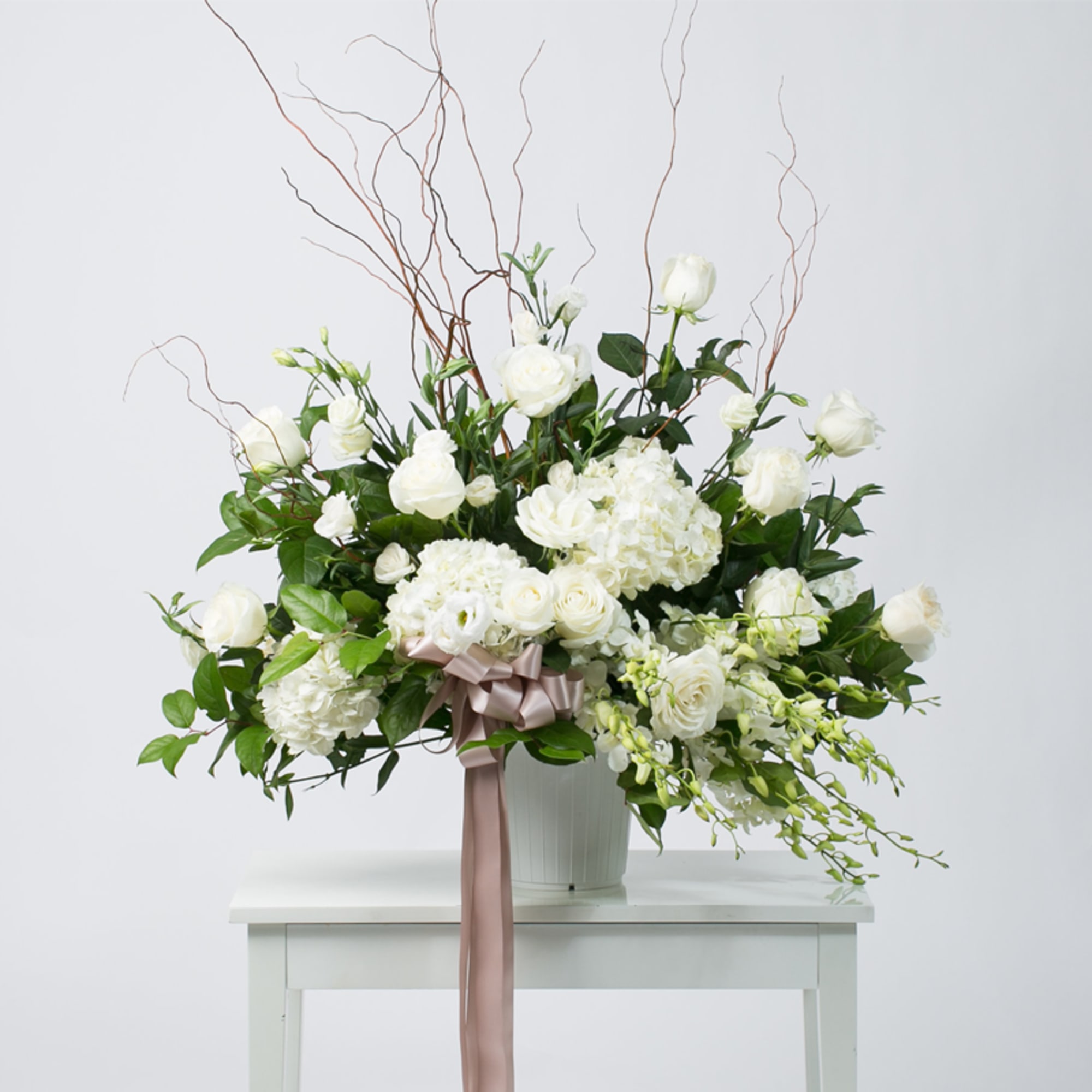 White floral arrangement in a vase with a pink ribbon