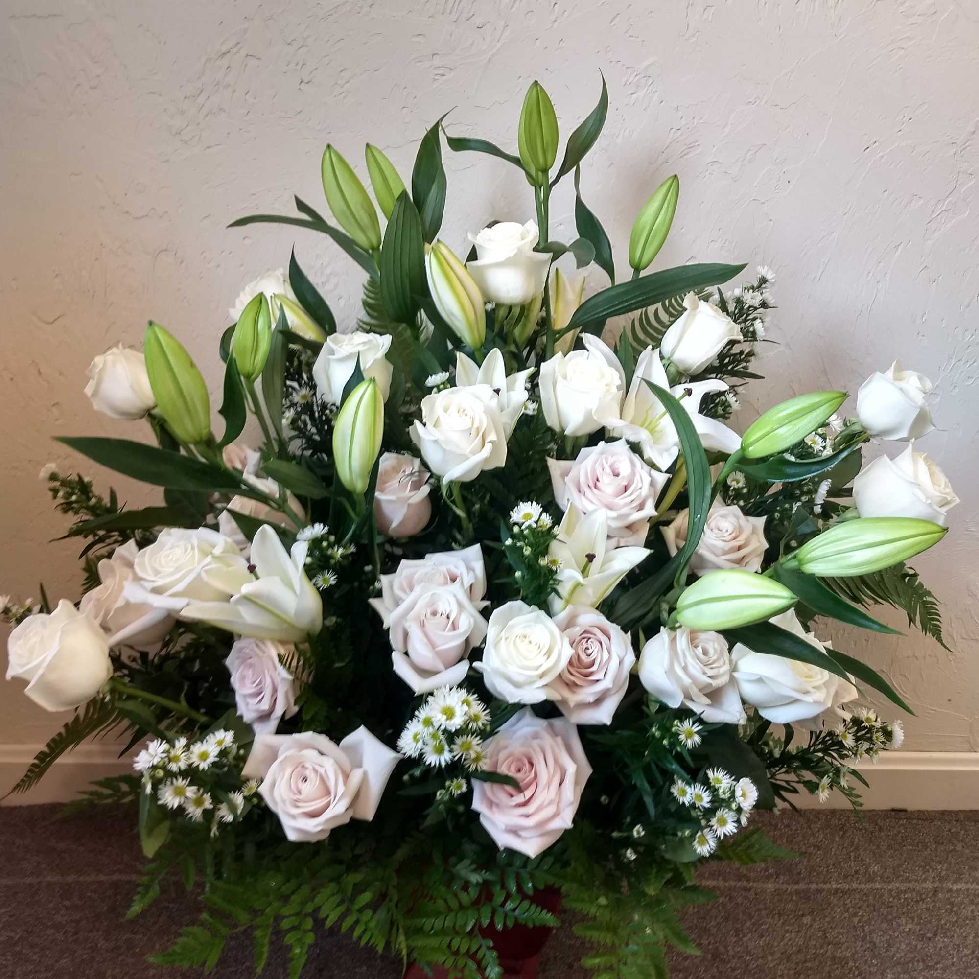 Large bouquet of white roses and lilies with green buds in a red container