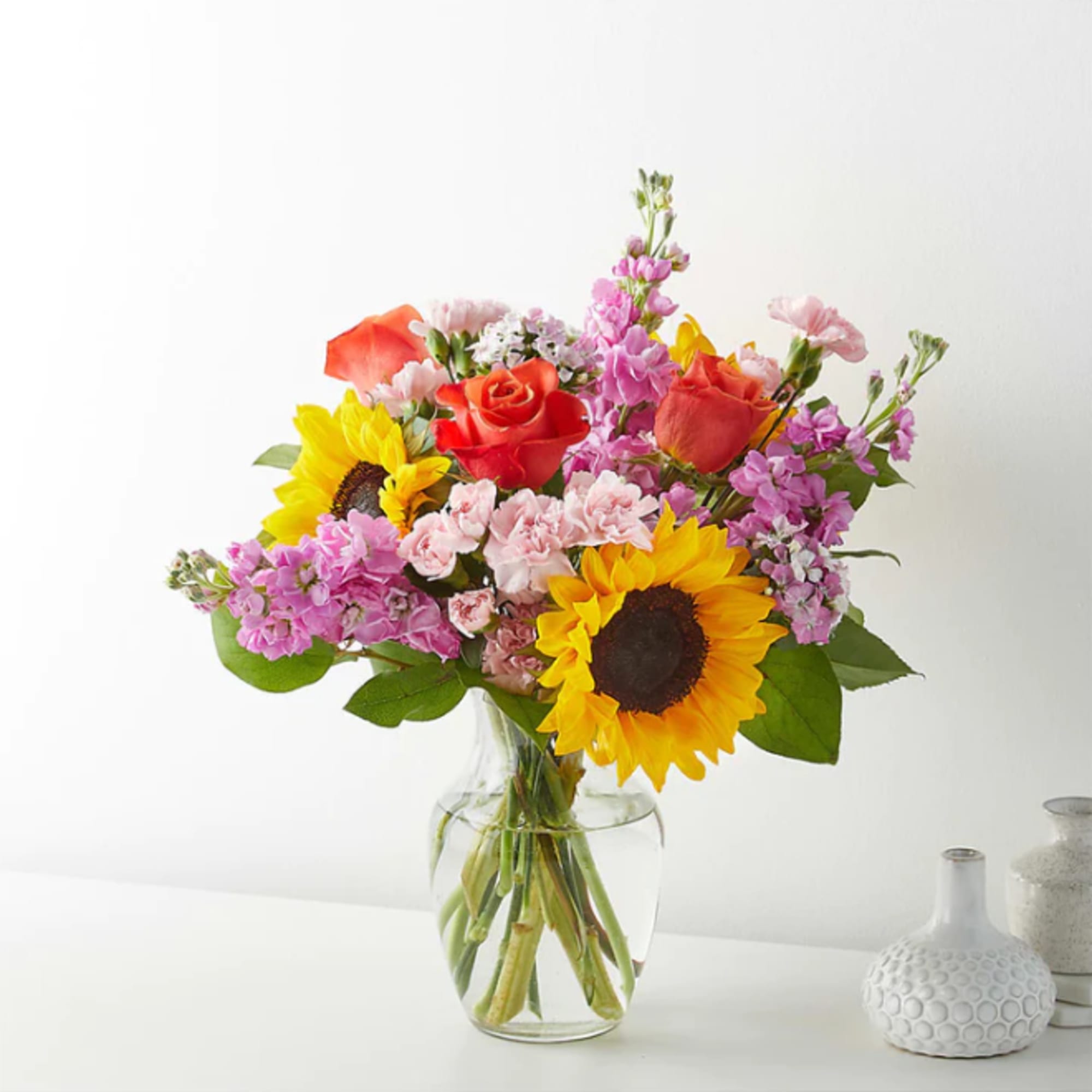 Mixed bouquet with sunflowers, roses, and pink blooms in a glass vase