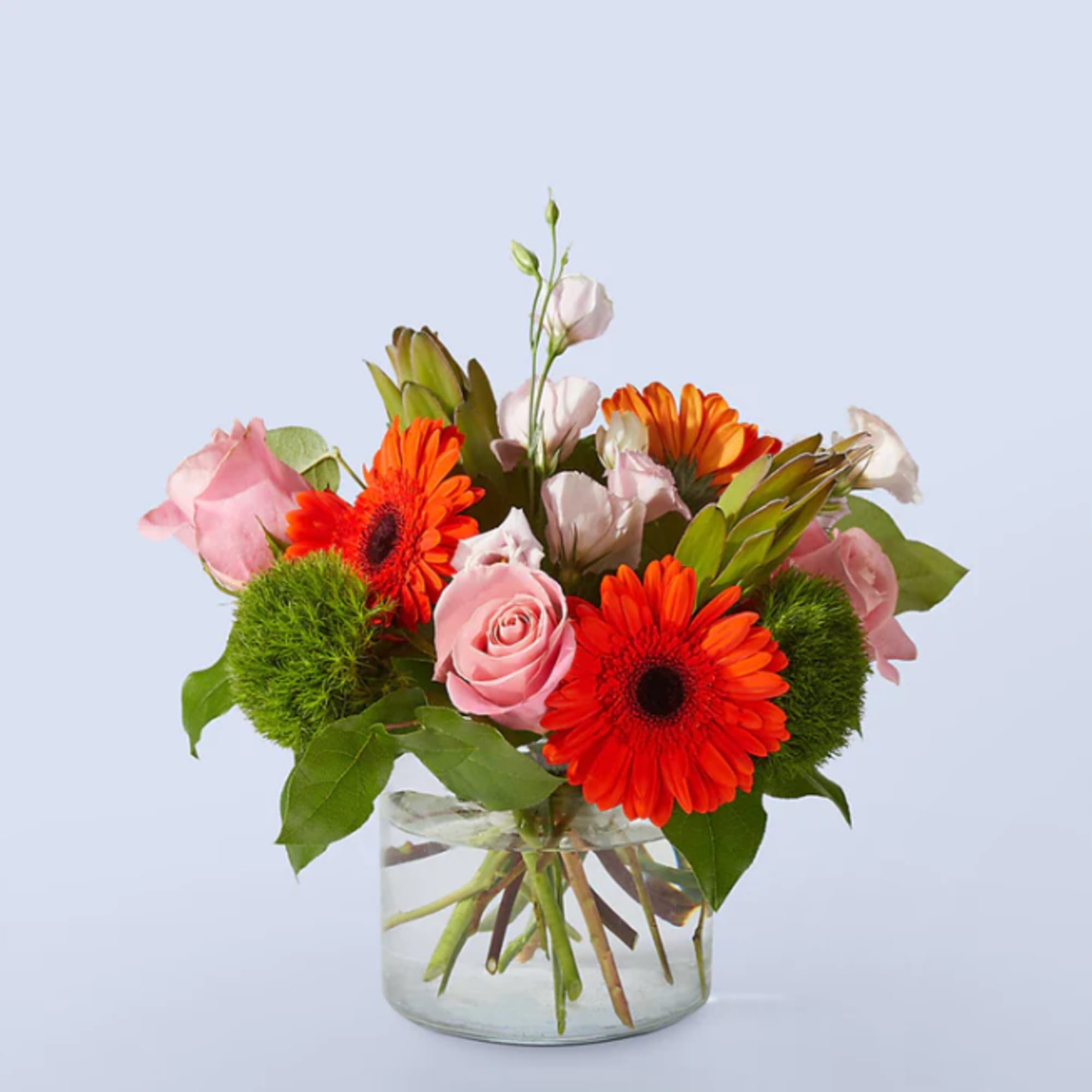 Pink roses and orange gerbera daisies in a clear glass vase