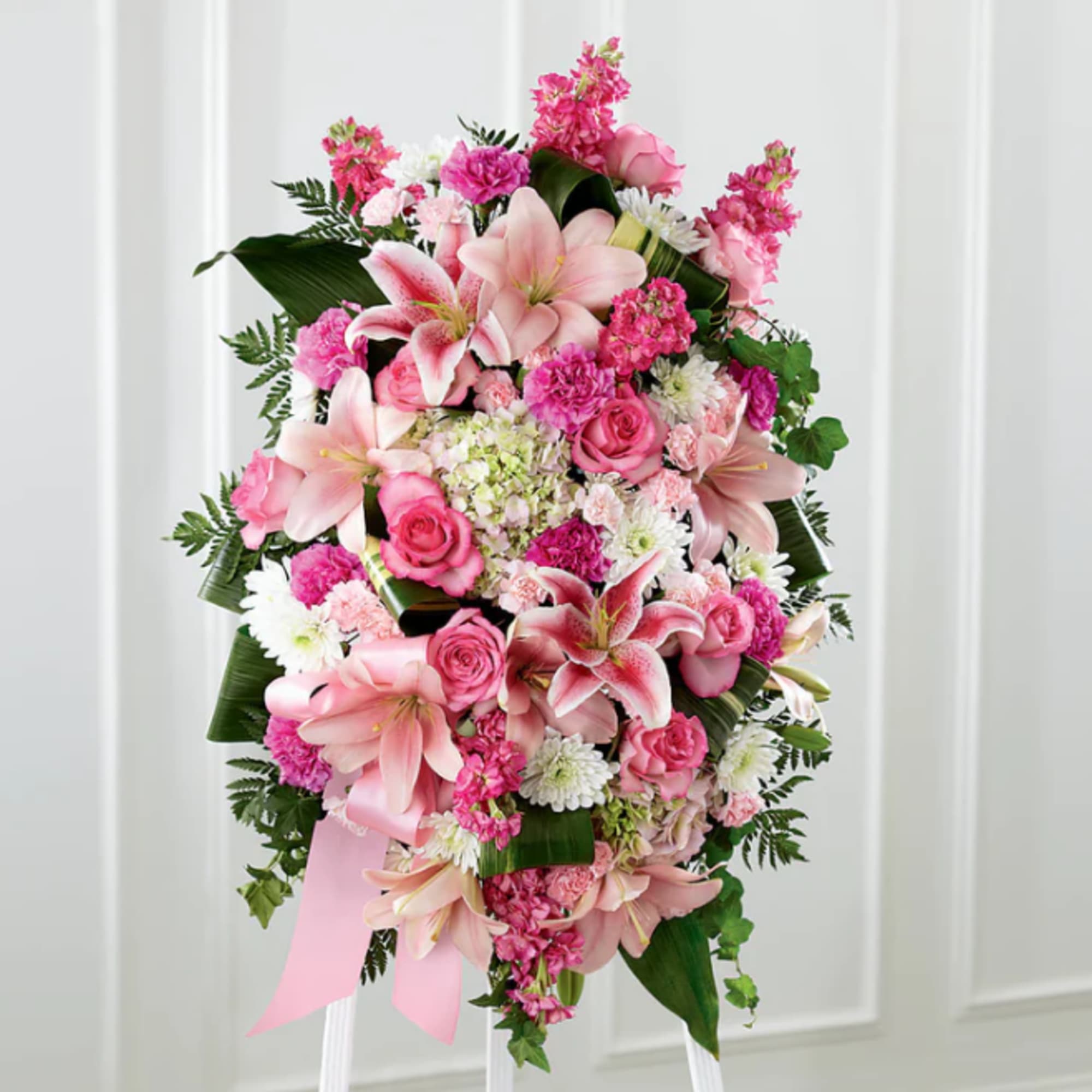 Pink and white funeral spray with lilies and roses on a stand