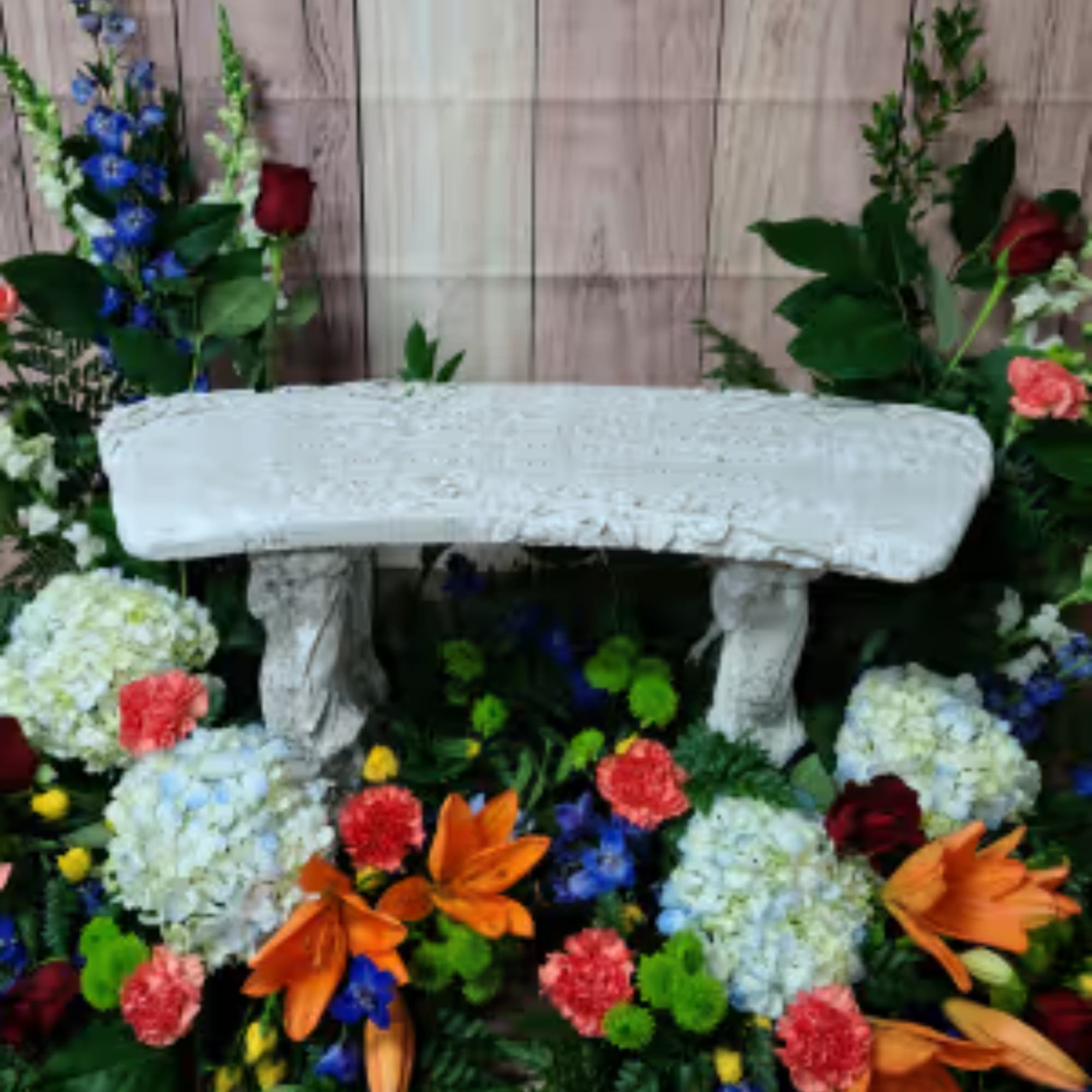 Floral arrangement around a white stone bench with mixed flowers.