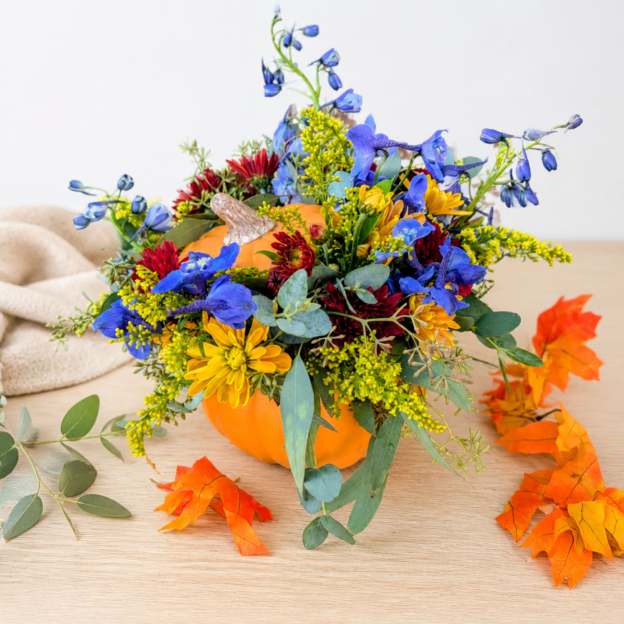 Pumpkin-shaped arrangement with blue, yellow, and red flowers