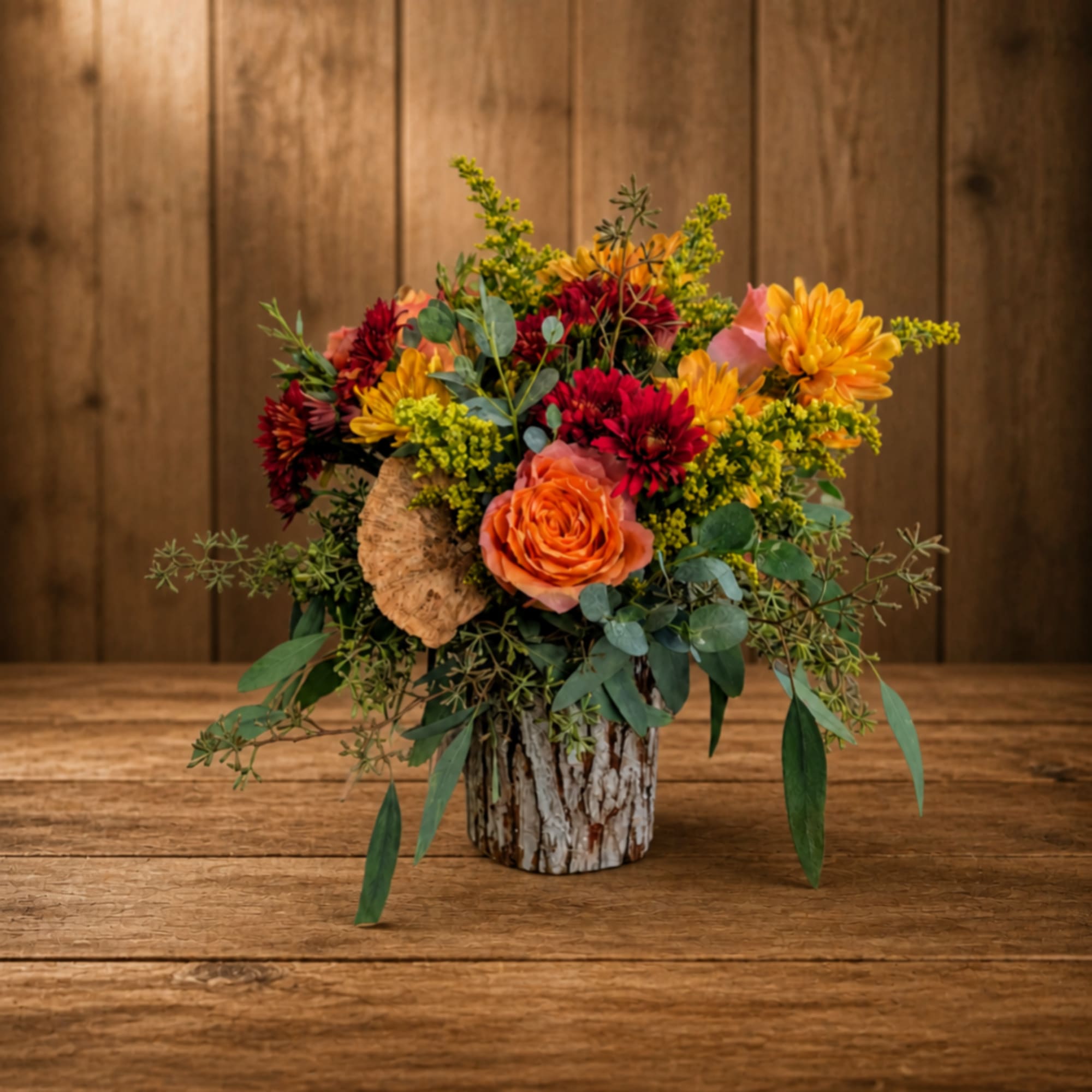 Mixed bouquet of orange, red, and yellow flowers in a rustic vase