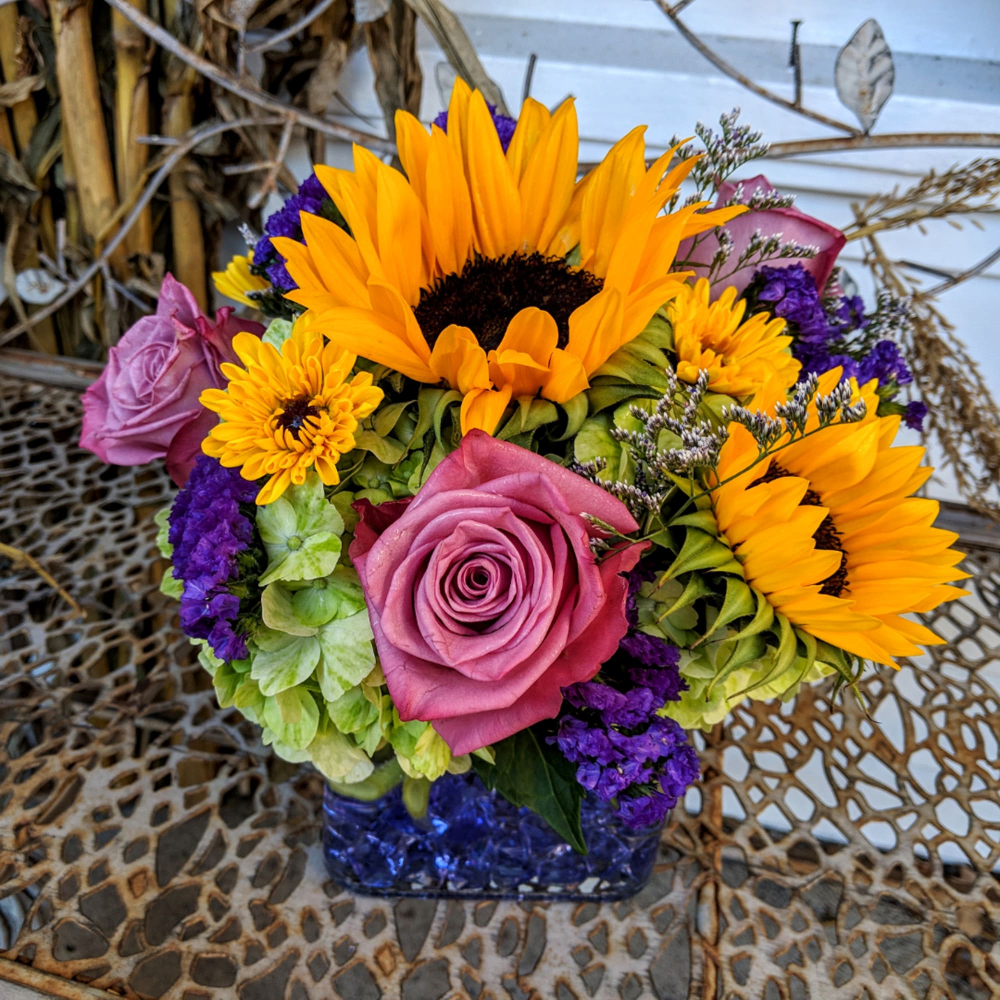 Bouquet of sunflowers, pink roses, and purple flowers in a blue glass vase